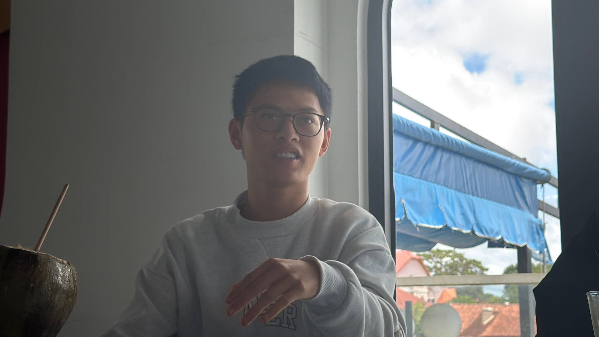 A contemplative moment at a modern rooftop venue in Đà Lạt with panoramic hillside views and architectural details including a blue awning and traditional Vietnamese landscape visible through floor-to-ceiling windows.