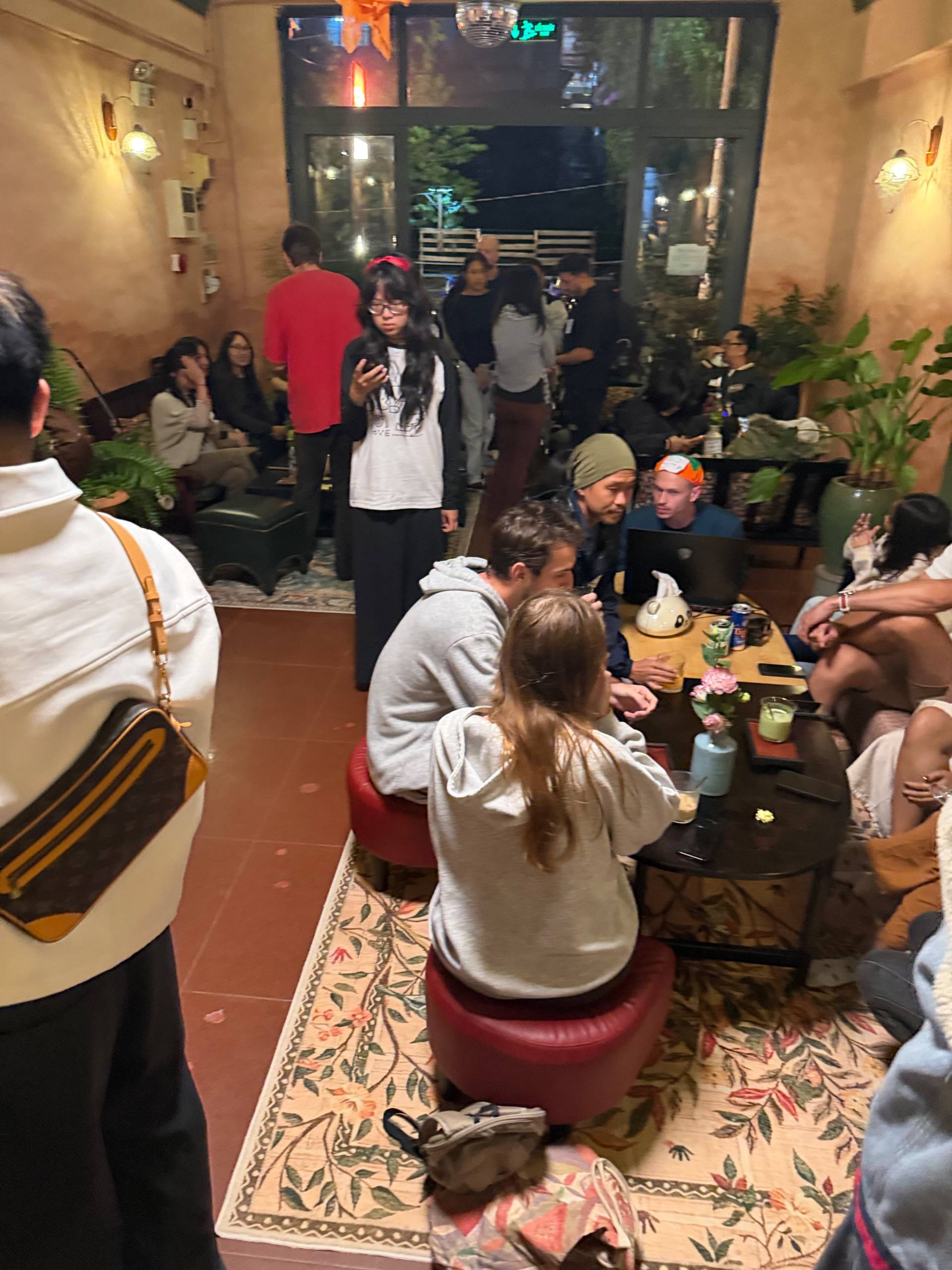 A lively gathering of friends in a cozy café in Đà Lạt, Vietnam, enjoying drinks and conversation around a table adorned with flowers and snacks.