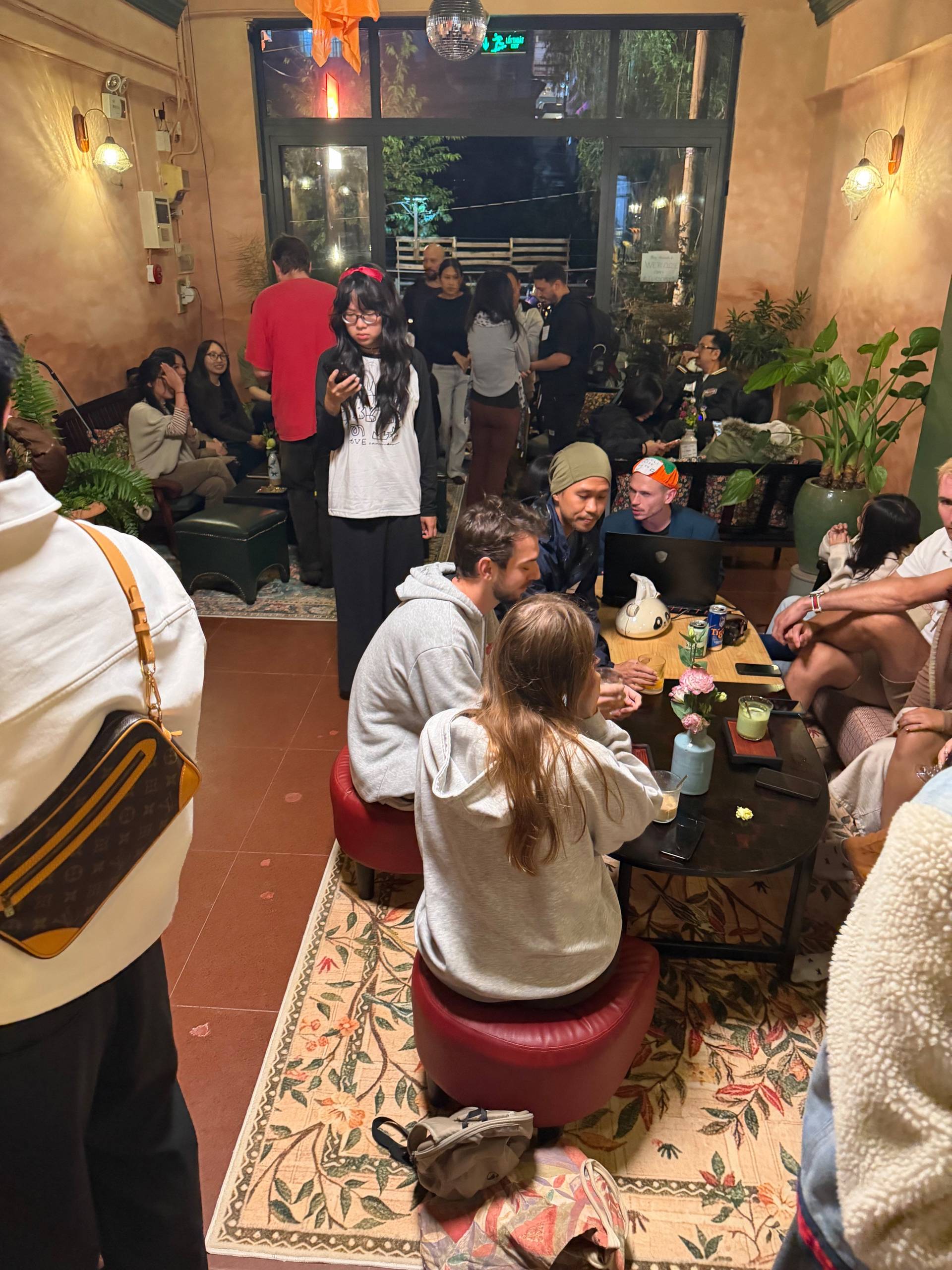 A lively gathering of friends in a cozy café in Đà Lạt, Vietnam, enjoying drinks and conversation under warm lighting.