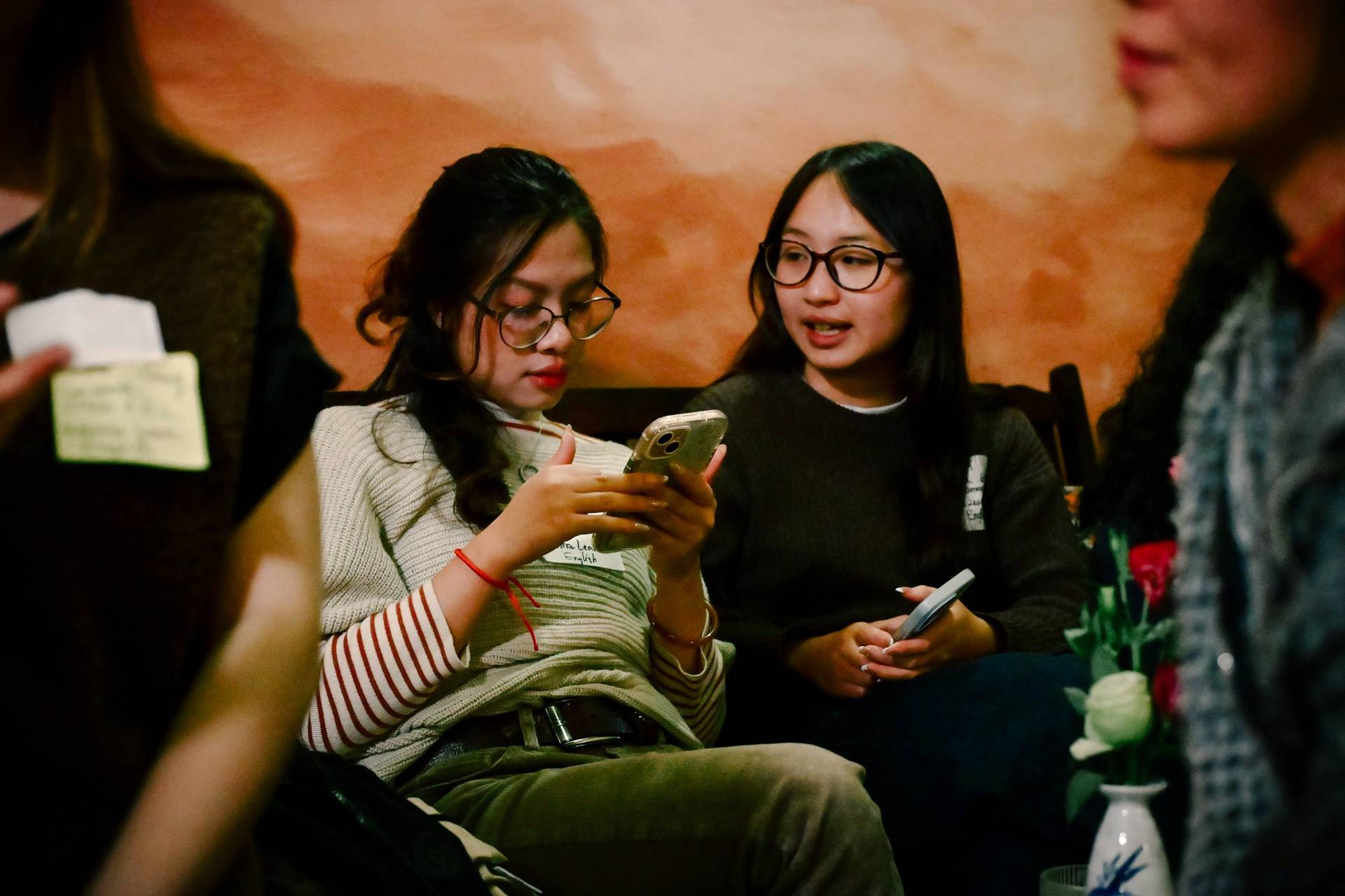 Two friends are engaged in a conversation while one looks at her phone during a social gathering in Đà Lạt, Vietnam.