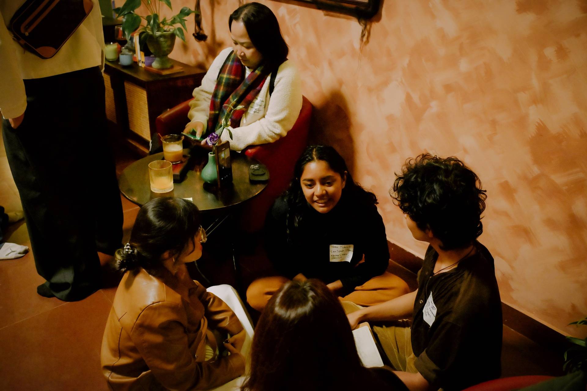 A group of friends gathered in a cozy café in Đà Lạt, Vietnam, engaging in lively conversation and enjoying drinks together under warm lighting.