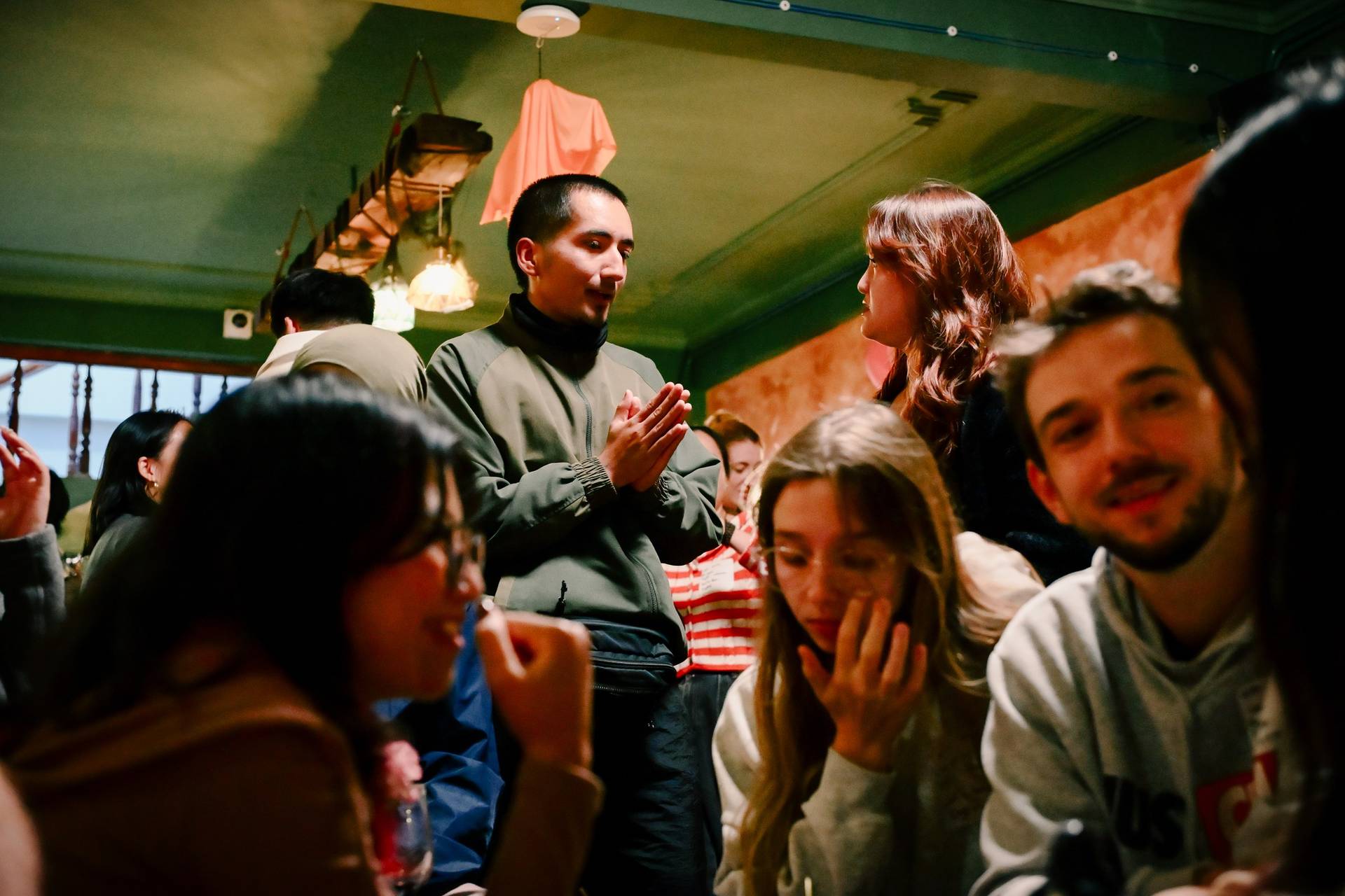 A lively gathering of friends in a cozy café in Đà Lạt, Vietnam, with warm lighting and green walls creating an intimate atmosphere.