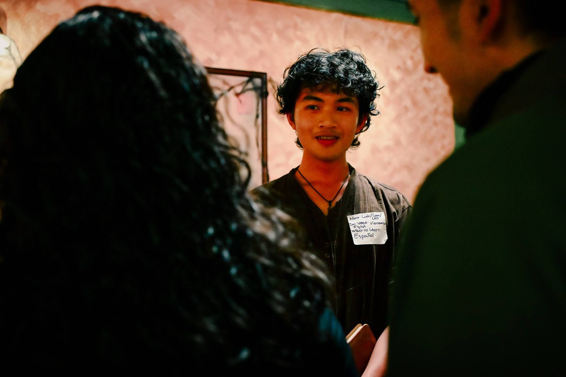A young man smiles warmly as he interacts with others in a social gathering in Đà Lạt, Vietnam, showcasing a vibrant and friendly atmosphere.