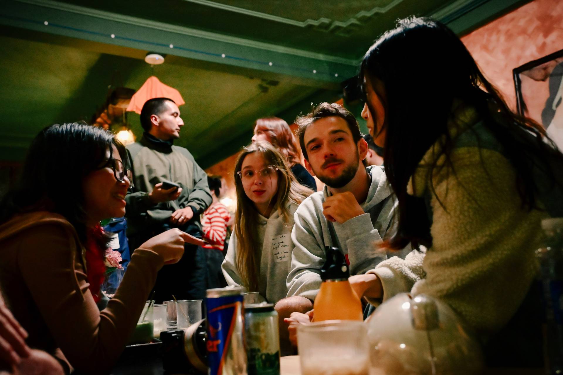 A lively gathering of friends in a cozy café in Đà Lạt, Vietnam, enjoying drinks and conversation under warm lighting.