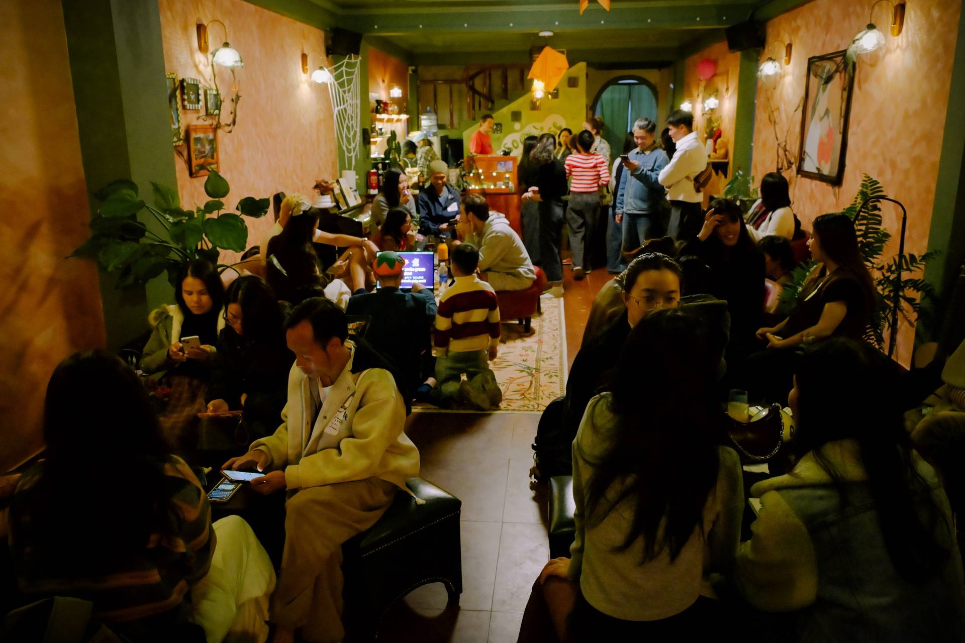 A lively gathering in a cozy café in Đà Lạt, Vietnam, with people engaged in various activities like chatting and using their phones.