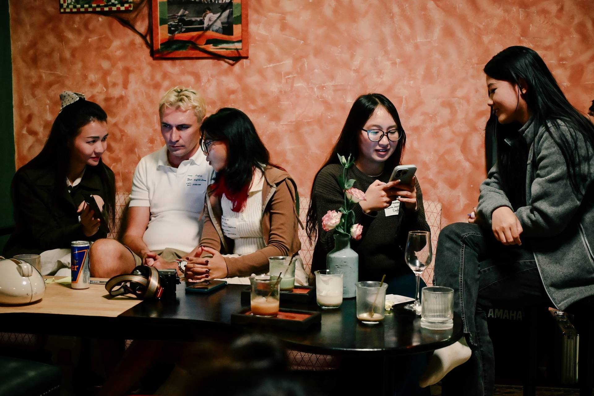 A group of friends gathered in a cozy café in Đà Lạt, Vietnam, enjoying drinks and engaging with their phones amidst a warm, intimate setting.
