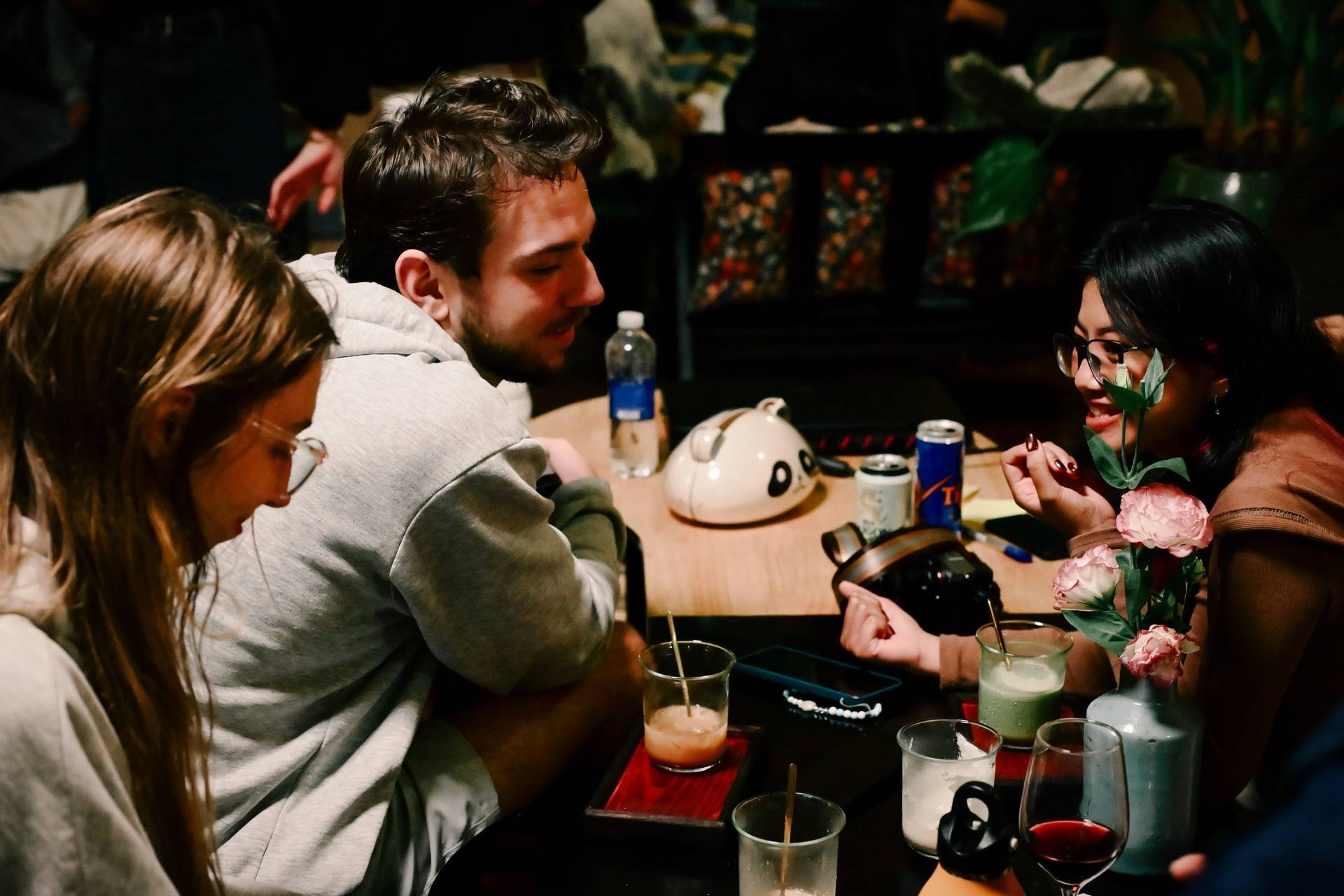 A group of friends enjoys a cozy evening in Đà Lạt, Vietnam, sharing drinks and laughter around a table adorned with flowers and snacks.