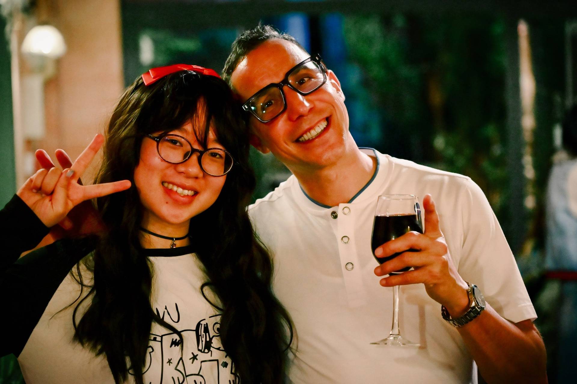 Two individuals share a joyful moment in Đà Lạt, Vietnam, with one making a peace sign and both holding drinks, suggesting a festive gathering.