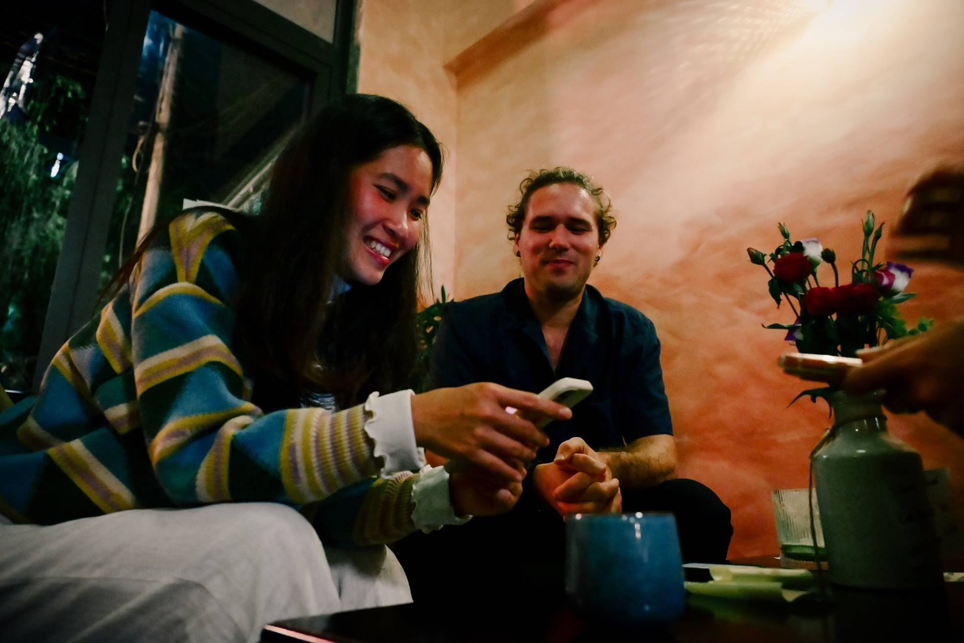Two individuals share a joyful moment in a cozy café setting in Đà Lạt, Vietnam, surrounded by warm lighting and floral decorations.