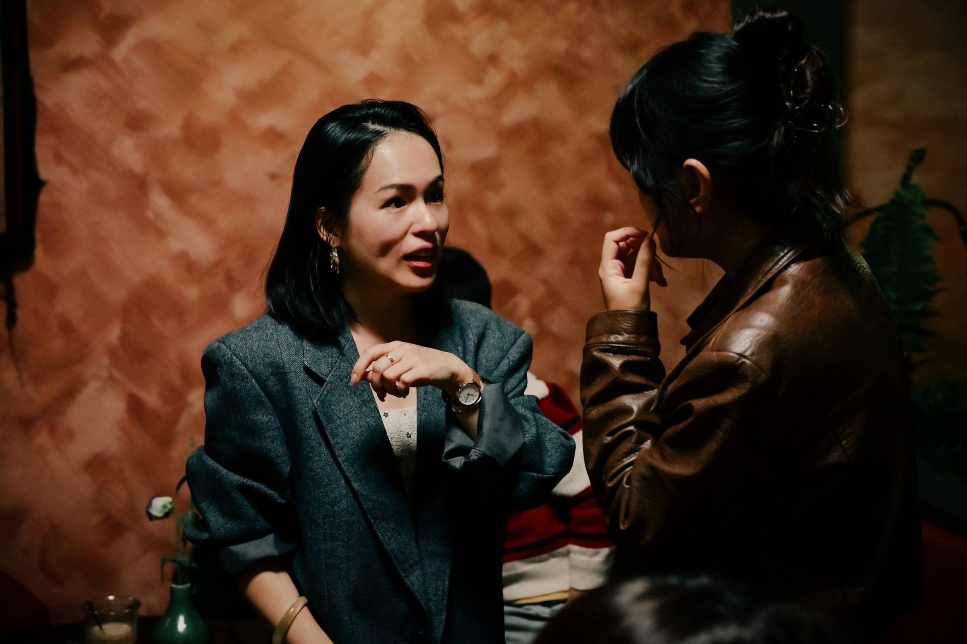 Two women engaged in a conversation in a dimly lit café setting with warm tones and rustic decor, suggesting a cozy and intimate atmosphere.