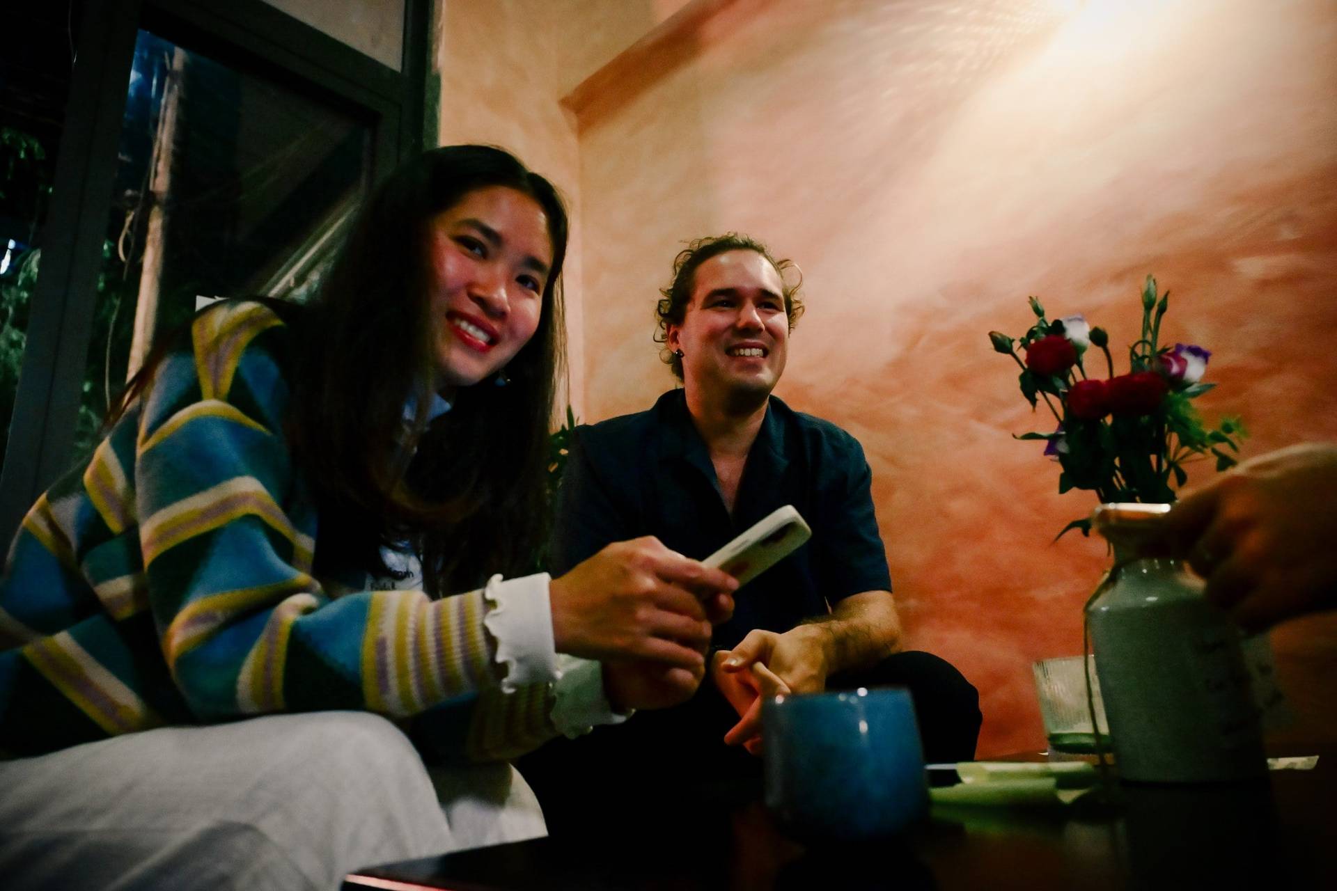 Two friends share a joyful moment over drinks in a cozy café setting in Đà Lạt, Vietnam.