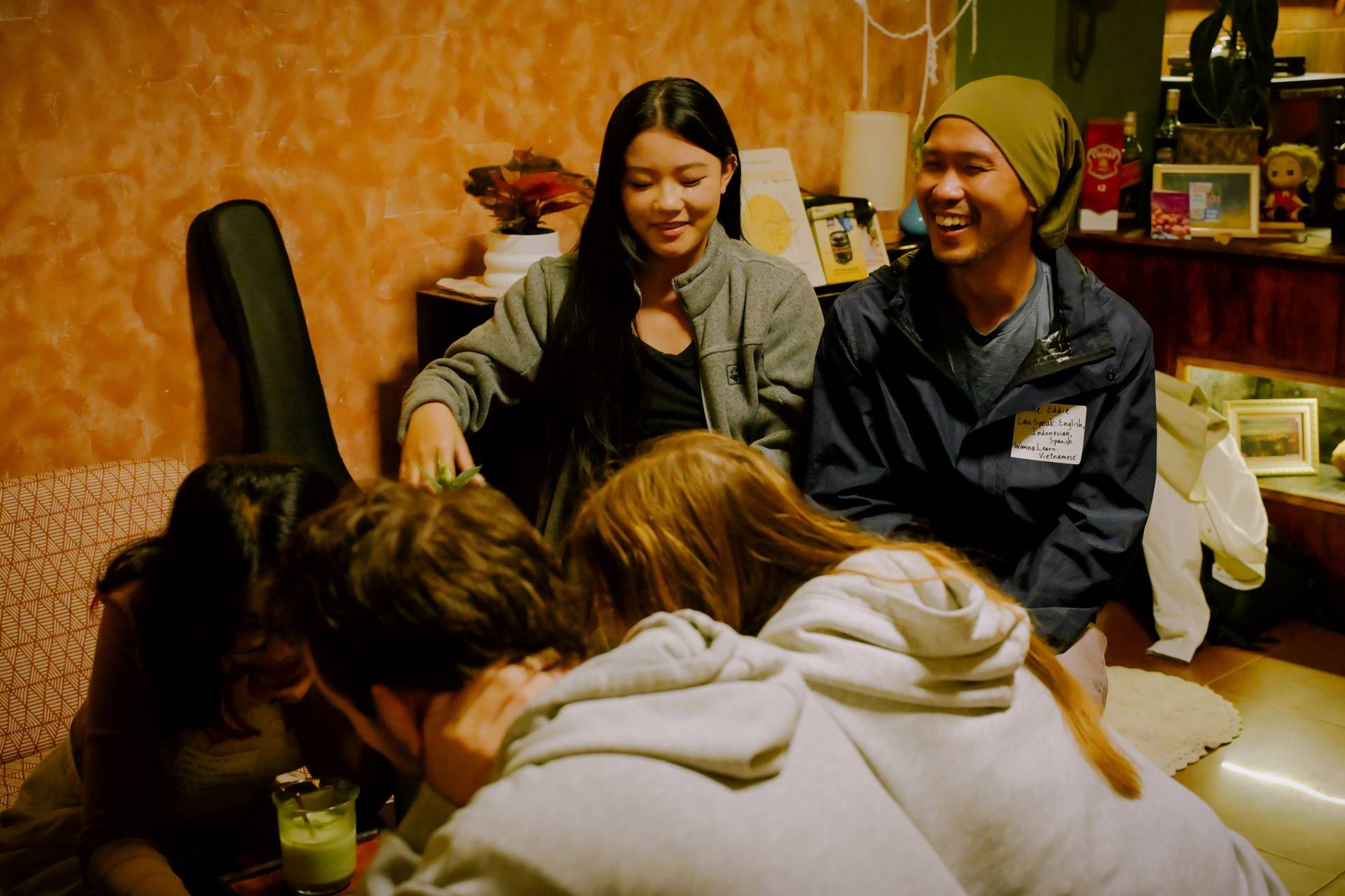 A group of friends gather in a cozy living room in Đà Lạt, Vietnam, laughing and enjoying each other's company over casual conversation.