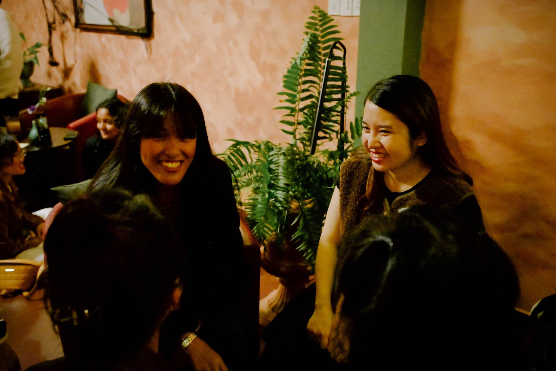 A group of friends share laughter in a cozy café setting in Đà Lạt, Vietnam, surrounded by warm lighting and greenery.