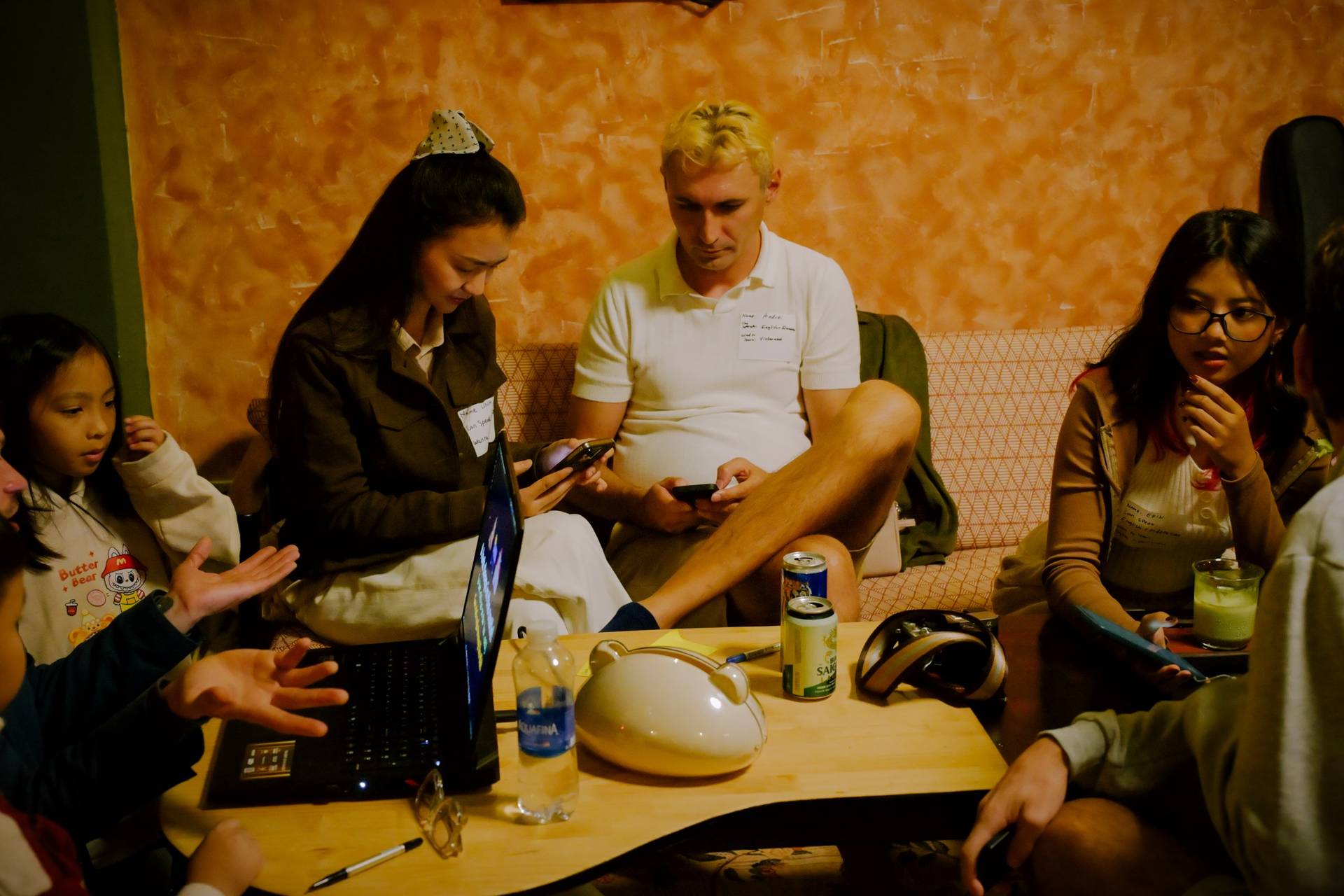 A group of friends gathered in a cozy café in Đà Lạt, Vietnam, engaging with technology and enjoying casual drinks while chatting and laughing.