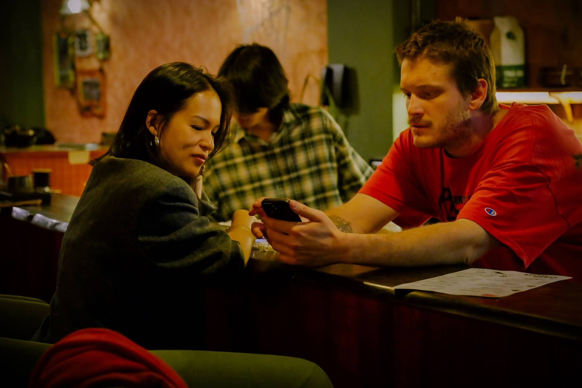 Two individuals are seated at a table in a cozy café in Đà Lạt, Vietnam, engrossed in their smartphones amidst a relaxed and intimate atmosphere.