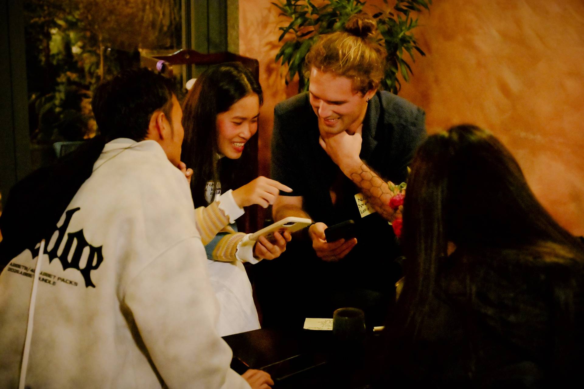 A group of friends gathered around a table in Đà Lạt, Vietnam, sharing laughter and enjoying each other's company while looking at something on their phones.