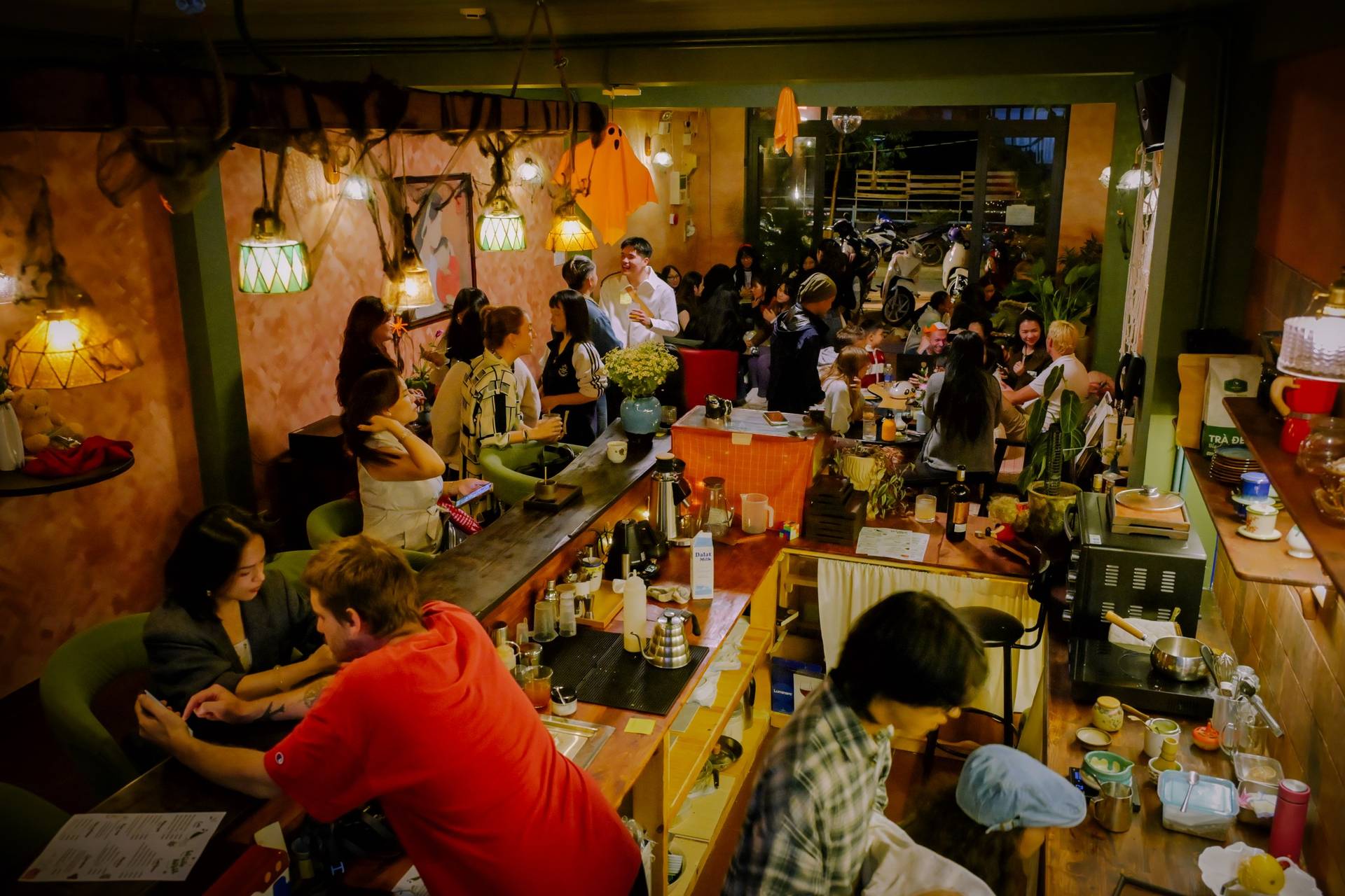 A lively gathering in a cozy café in Đà Lạt, Vietnam, with patrons enjoying drinks and conversation under warm ambient lighting.
