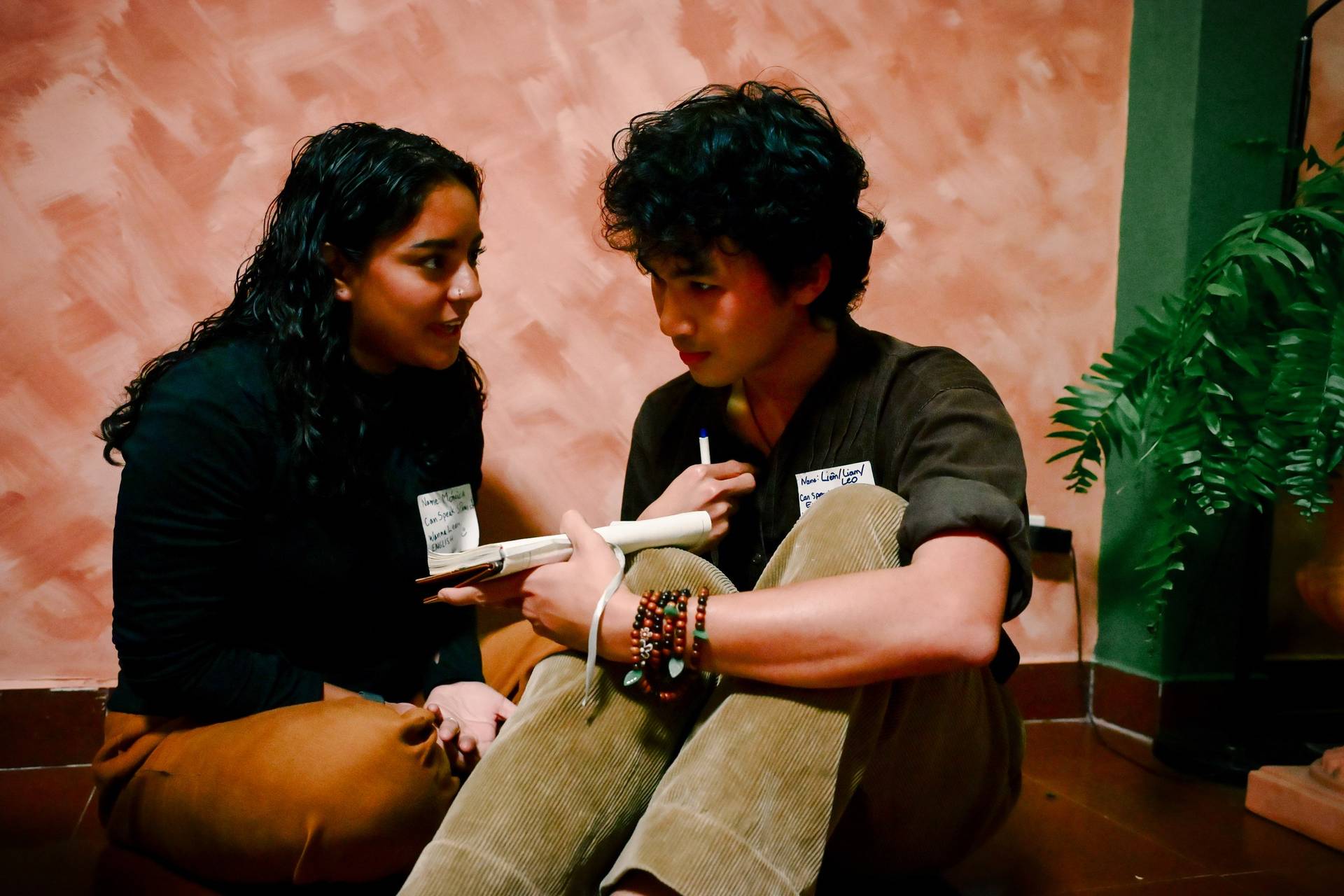Two individuals engaged in a conversation during what appears to be a cultural or educational event in Đà Lạt, Vietnam, with name tags indicating their names and language abilities.