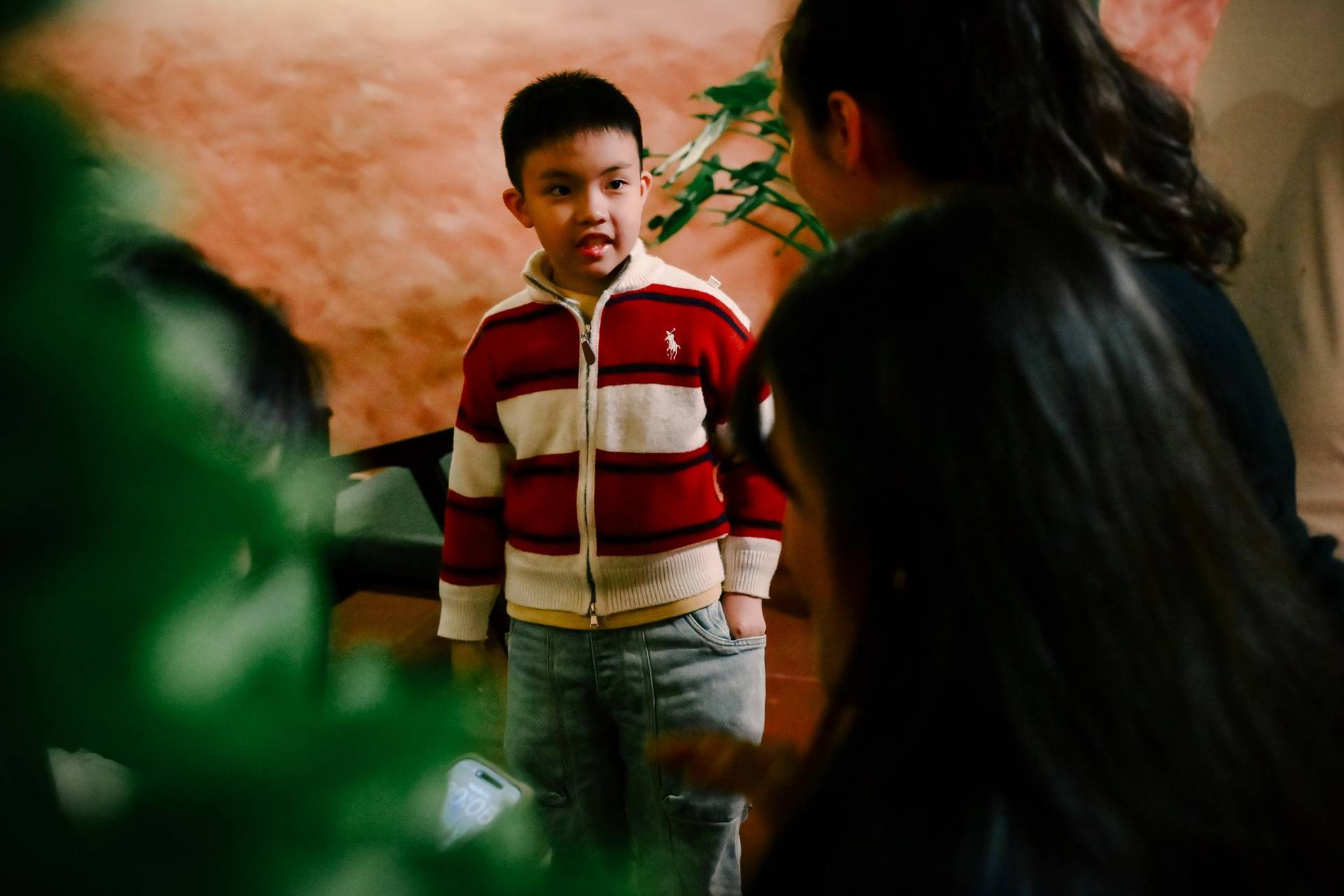 A young boy in a striped sweater stands amidst adults during what appears to be a social gathering or event in Đà Lạt, Vietnam.
