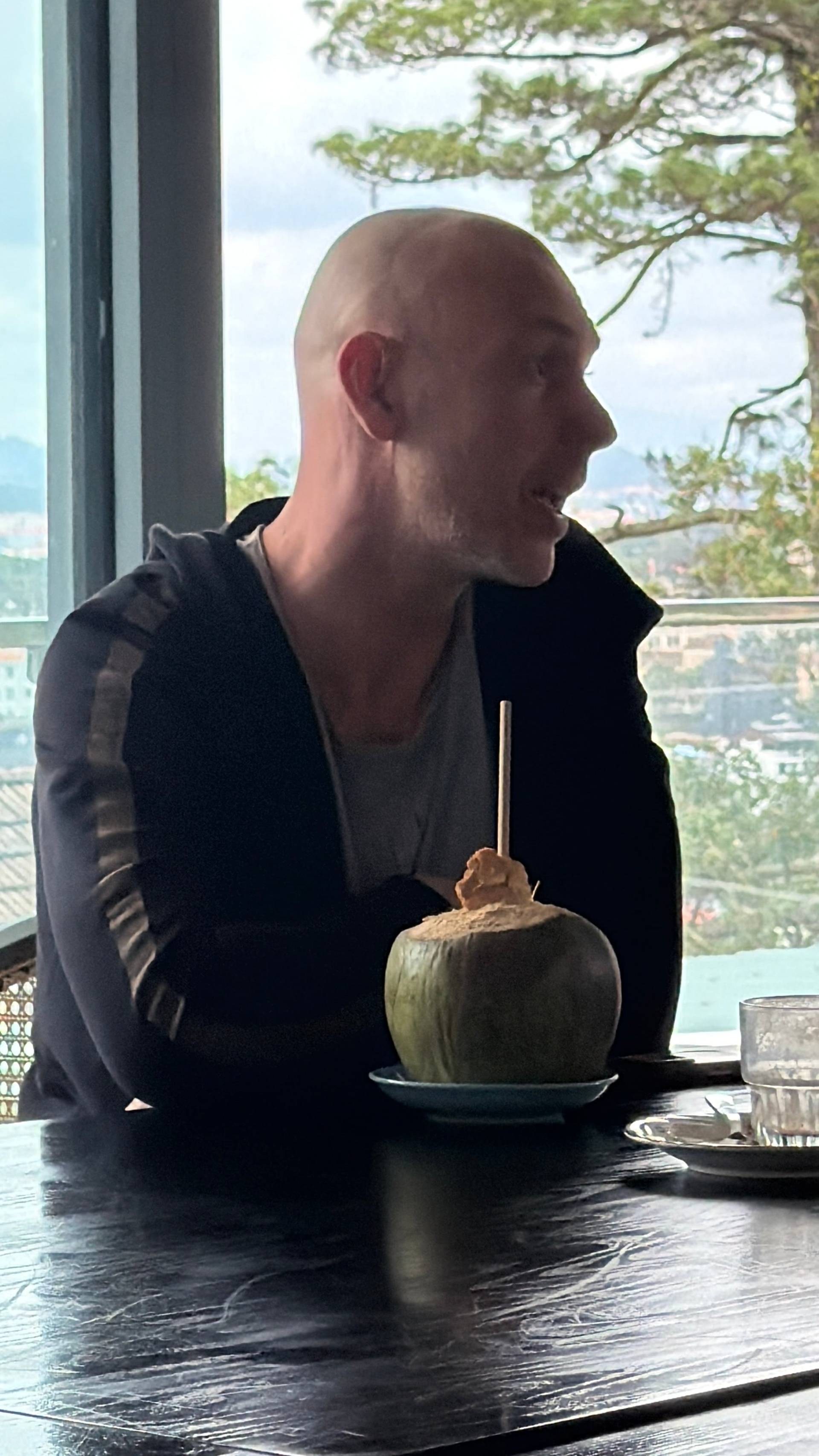 Refreshing moment at a Đà Lạt mountain-top event venue, enjoying fresh coconut drink while overlooking the pine-forested highlands and distant cityscape