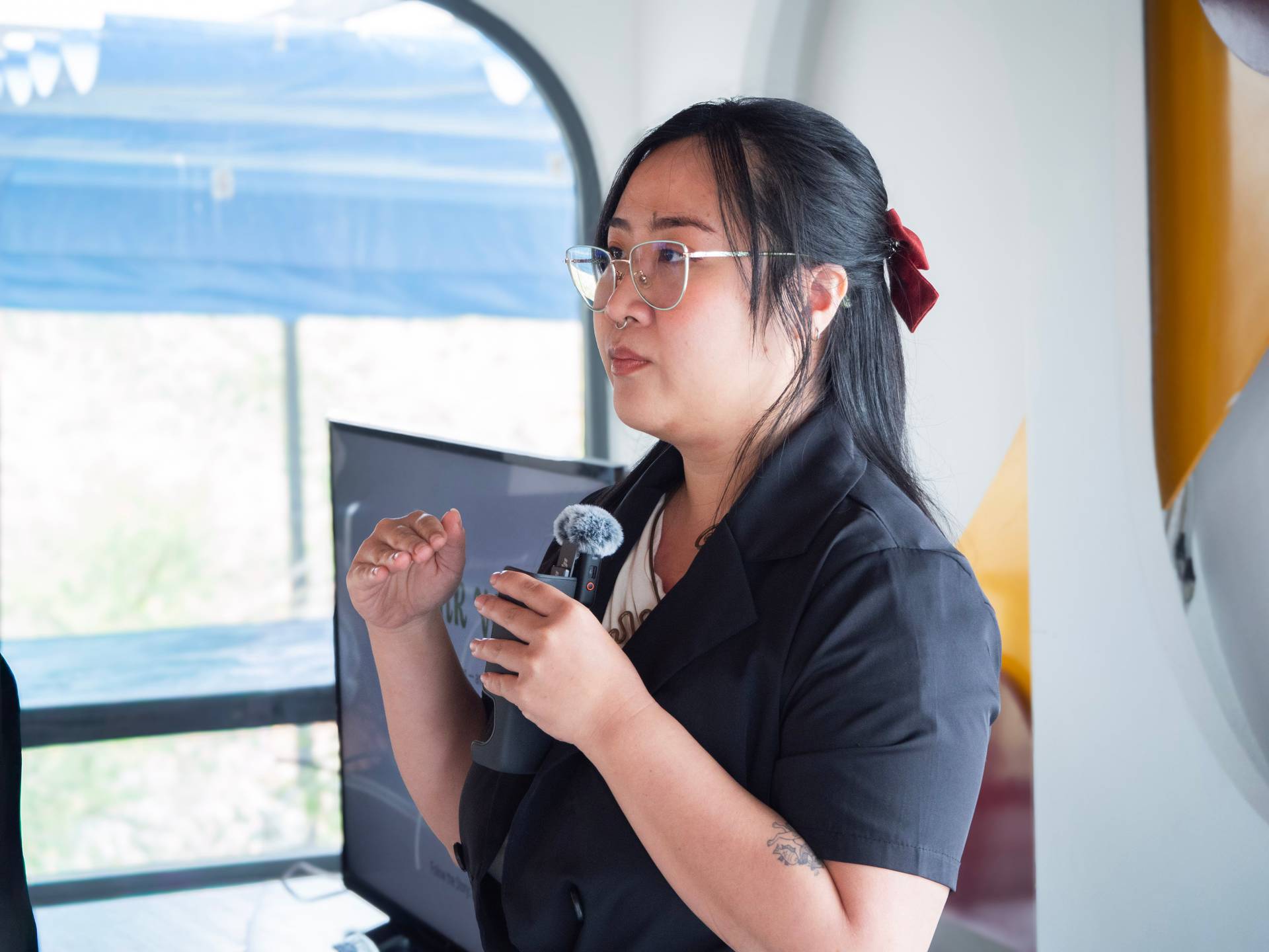 A speaker presents at the Dalat Build hackathon, delivering a talk near a panoramic window overlooking the scenic Đà Lạt hillside landscape.