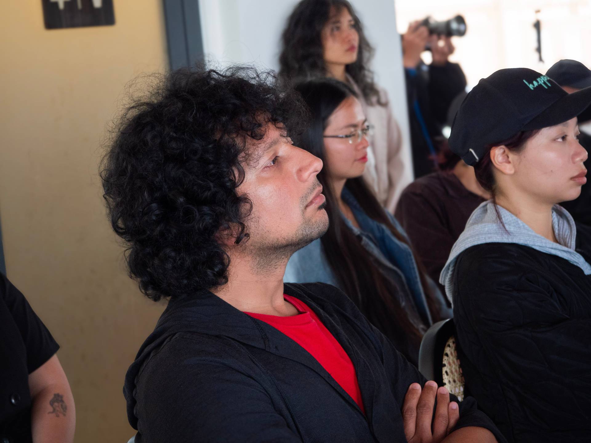 Attendees at the Dalat Build hackathon watch a live presentation or demo, gathered in the modern event venue with industrial-style architecture and accent lighting.