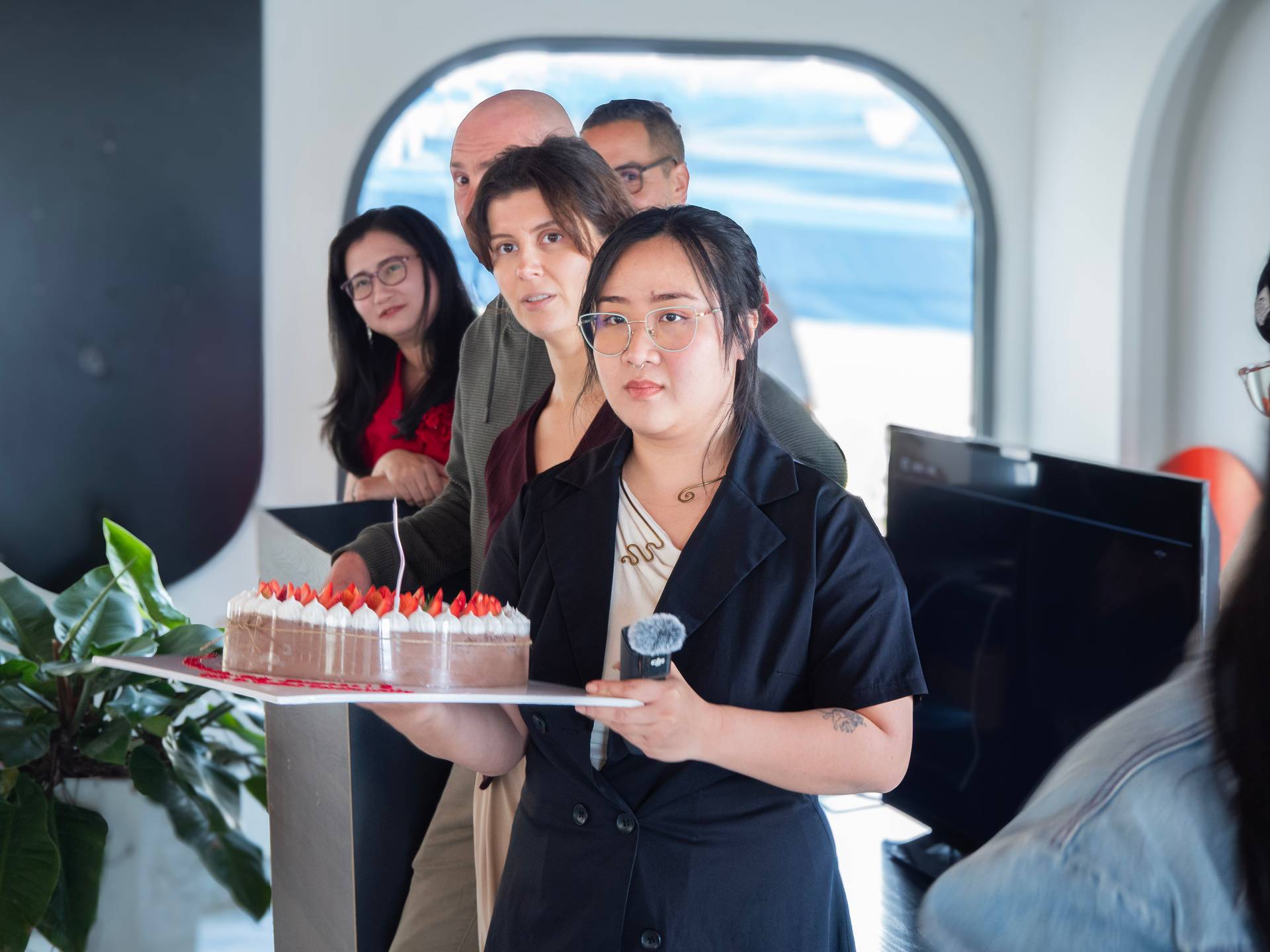 Event participants celebrate at an indoor venue in Đà Lạt with a scenic mountain view, featuring a fresh strawberry cake during a festive gathering moment.