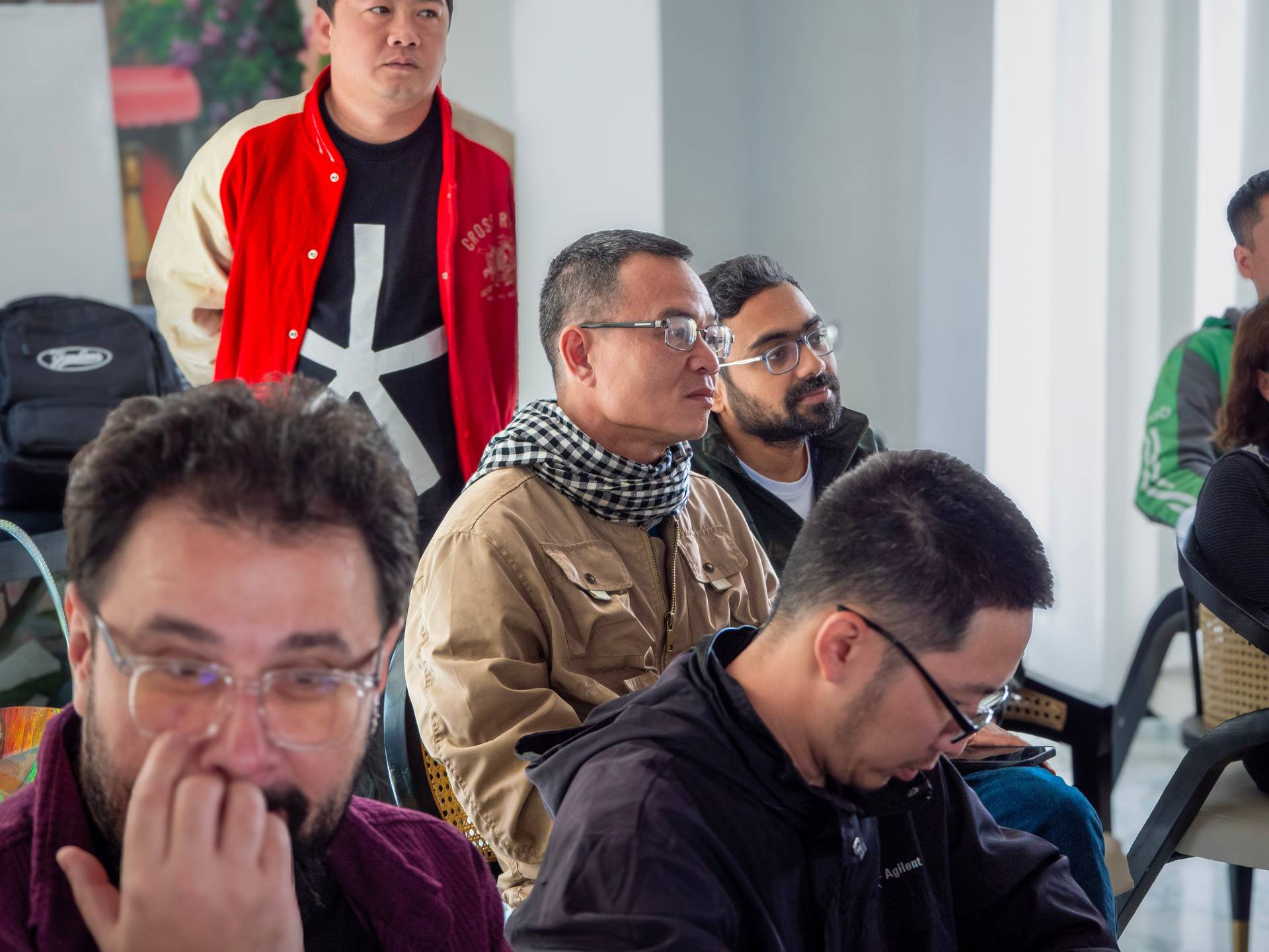 Diverse group of attendees gathered in a modern white interior space during a community tech event, showing mixed-age participation and engagement.