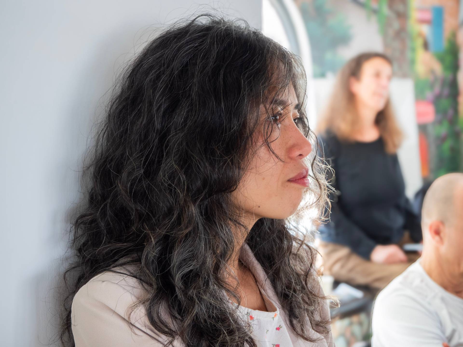 Profile view of an engaged listener at a community event, with colorful event decoration and diverse attendees visible in the background.