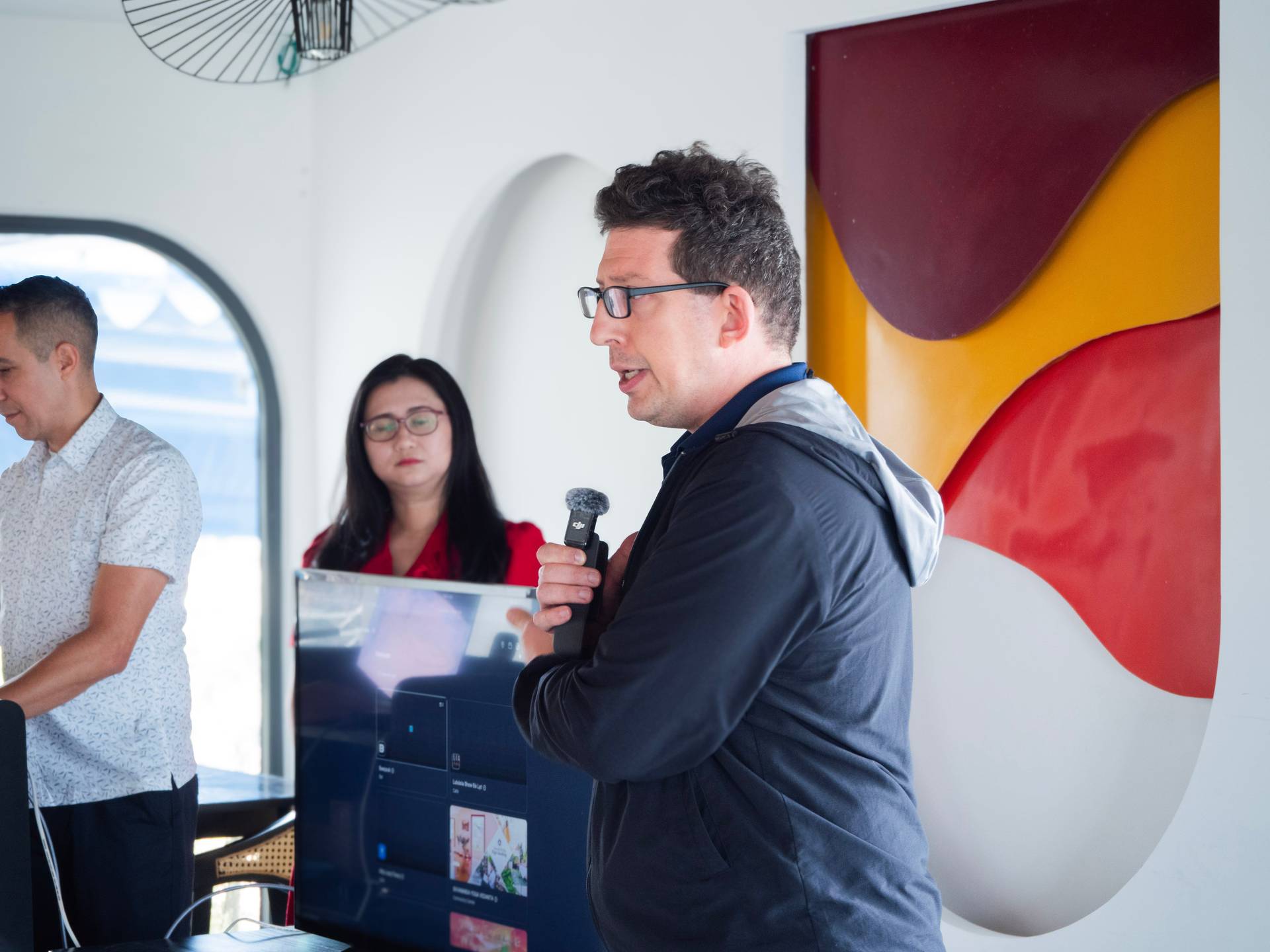Speaker presenting at a tech event in a modern venue with distinctive porthole window and colorful architectural elements.