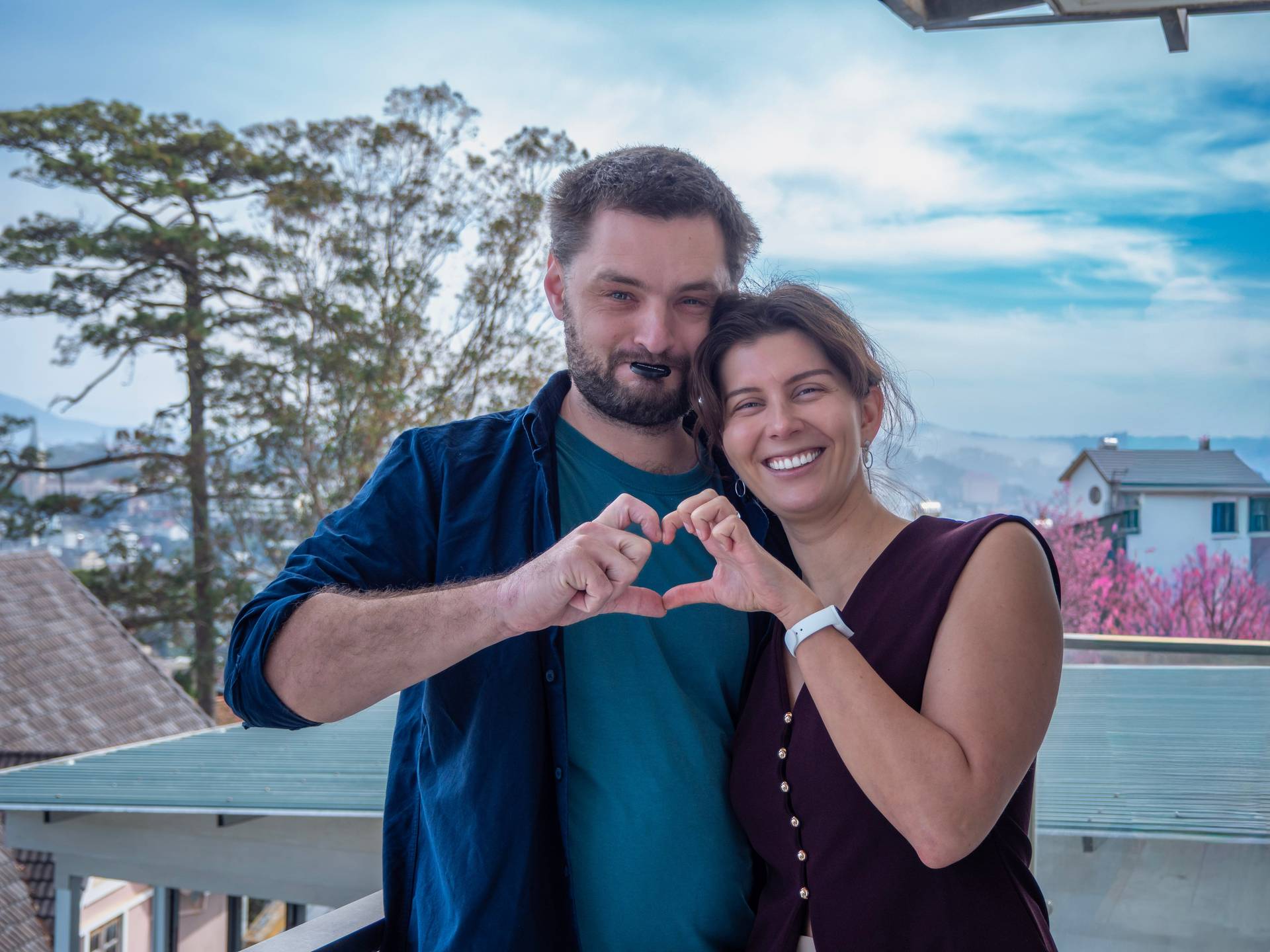 Romantic moment overlooking Đà Lạt's pine-forested highlands, with a heart gesture made against a scenic backdrop. Captures the romantic tourism appeal of Đà Lạt with blooming flowers and mountain vistas.