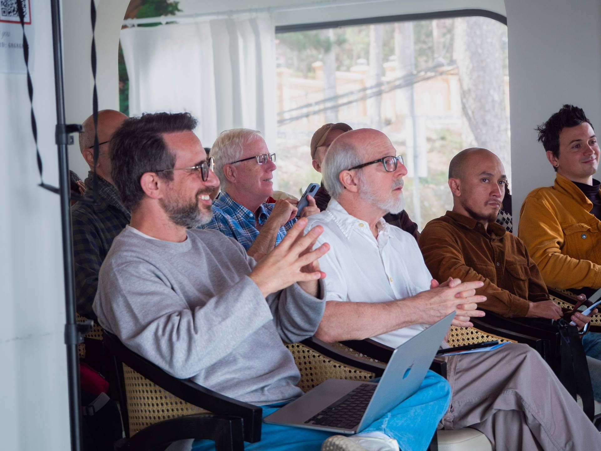 Diverse group of attendees seated in a bright modern indoor space, engaged with devices during a tech event or workshop presentation.