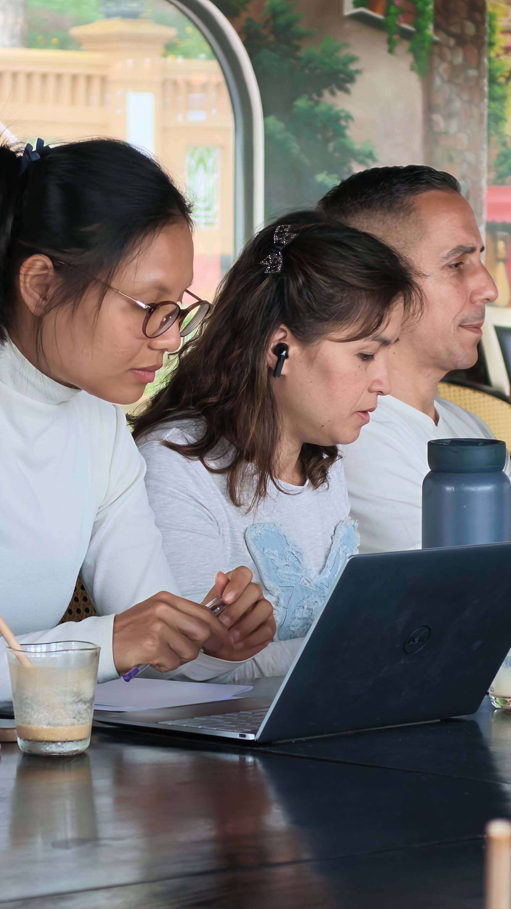 A group of individuals is engaged in a collaborative activity using laptops and writing materials at a café in Đà Lạt, Vietnam.