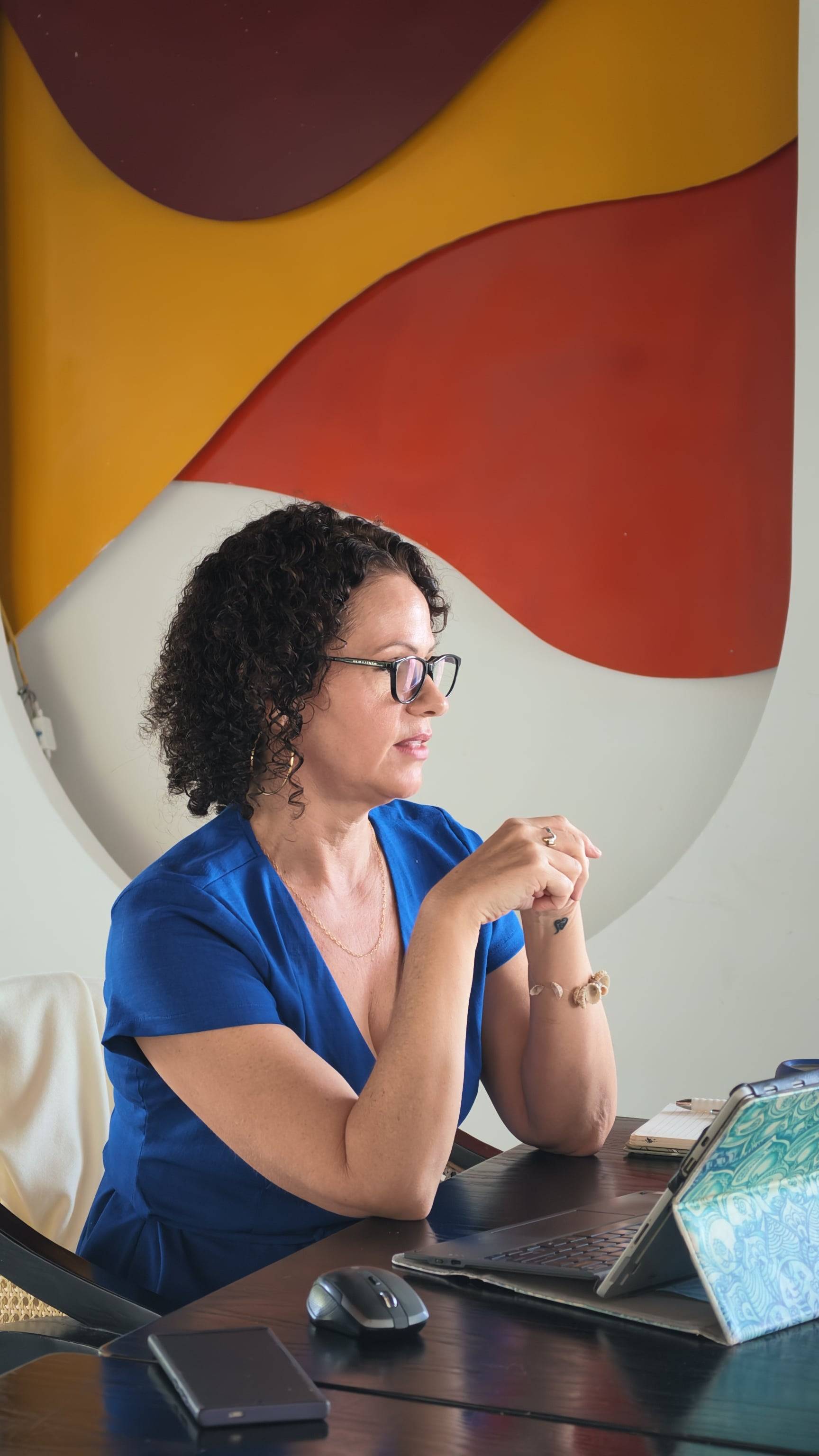 A woman is seated at a desk in a vibrant office setting with colorful abstract art in the background, suggesting a creative and professional environment.