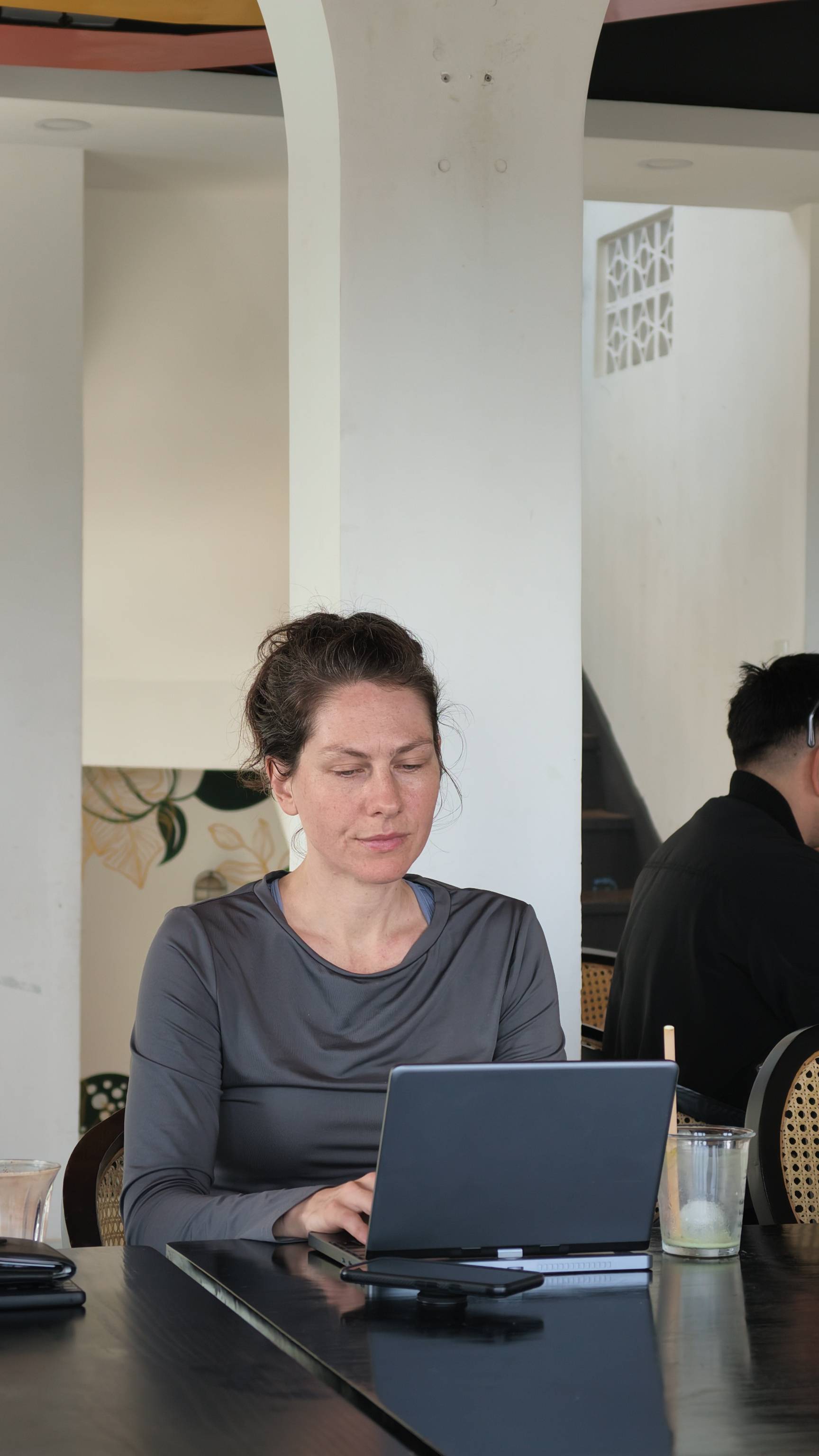 A woman is focused on her laptop in a cozy café setting in Đà Lạt, Vietnam, surrounded by modern decor and natural light.