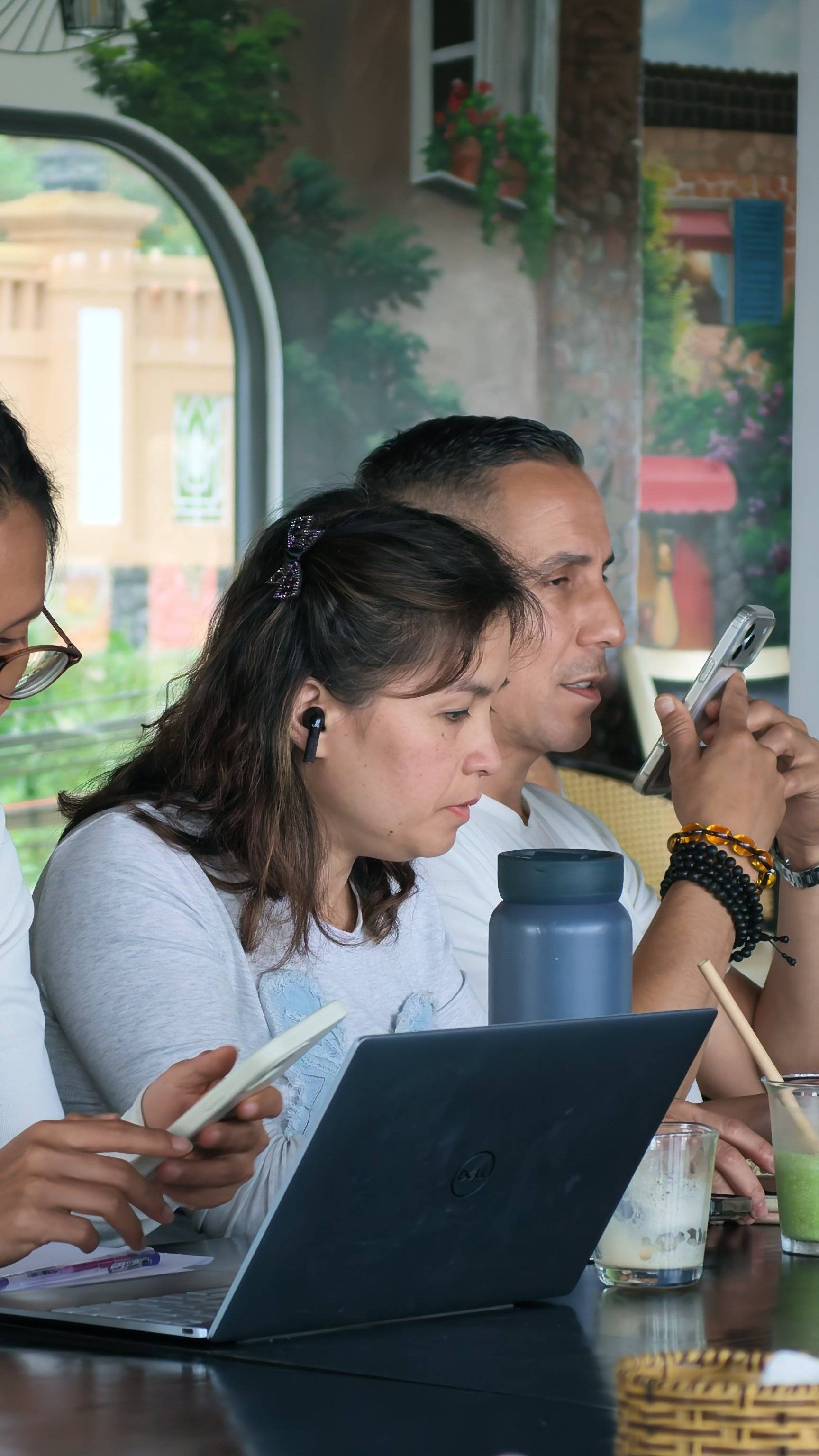 A group of individuals is gathered in a cozy café in Đà Lạt, Vietnam, engaged with their laptops and smartphones while enjoying beverages and snacks.