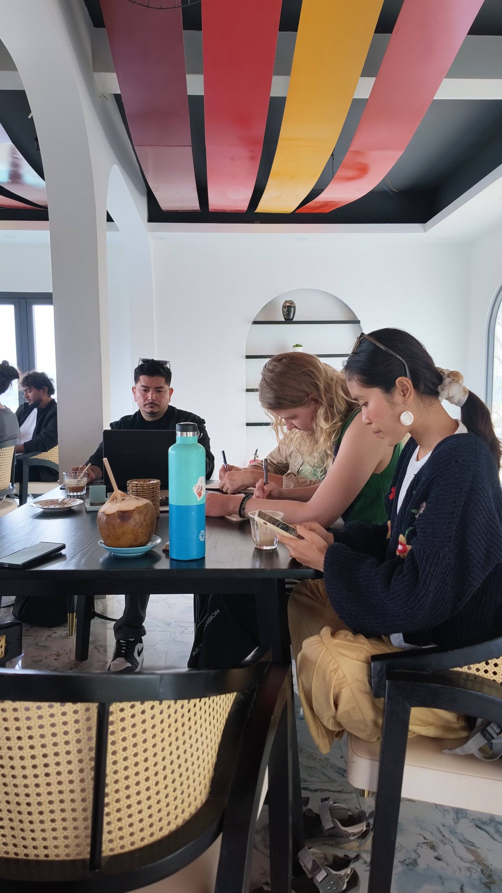 A group of individuals is engaged in a creative activity at a vibrant café in Đà Lạt, Vietnam, surrounded by colorful decor and modern furnishings.