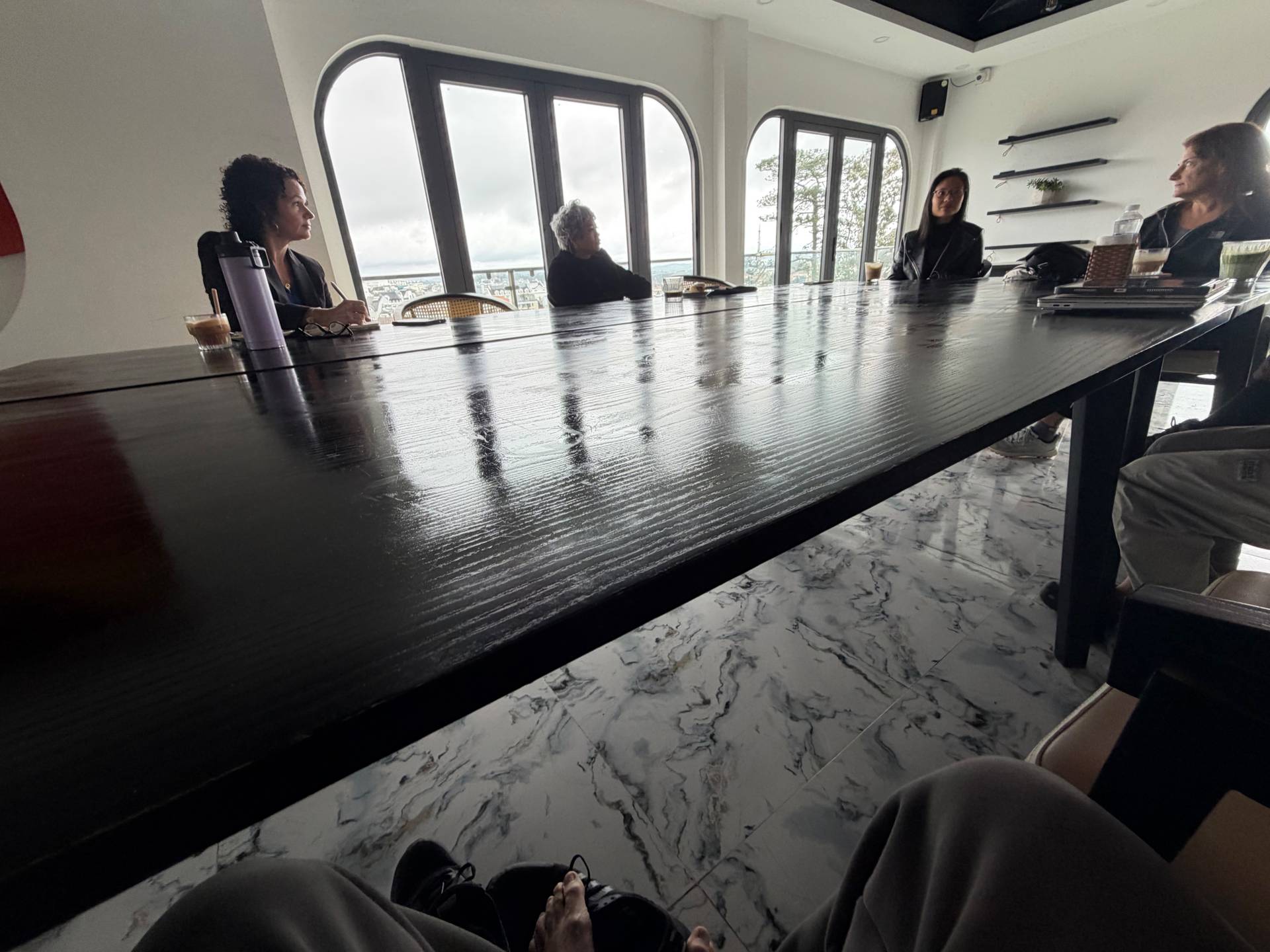 A group of individuals engaged in a meeting or discussion around a long table with a scenic view overlooking Đà Lạt's landscape.