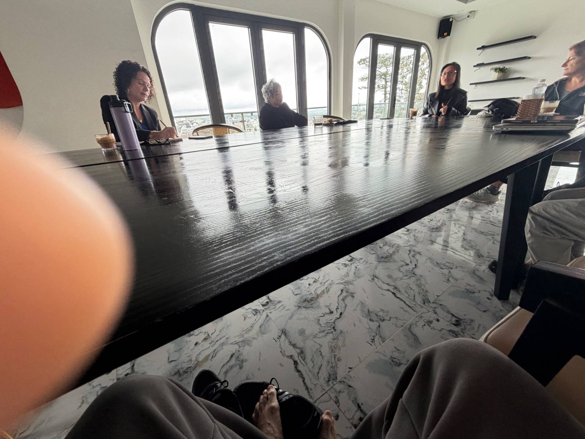 A group of individuals engaged in a meeting or discussion around a long table with a scenic view overlooking Đà Lạt's landscape.