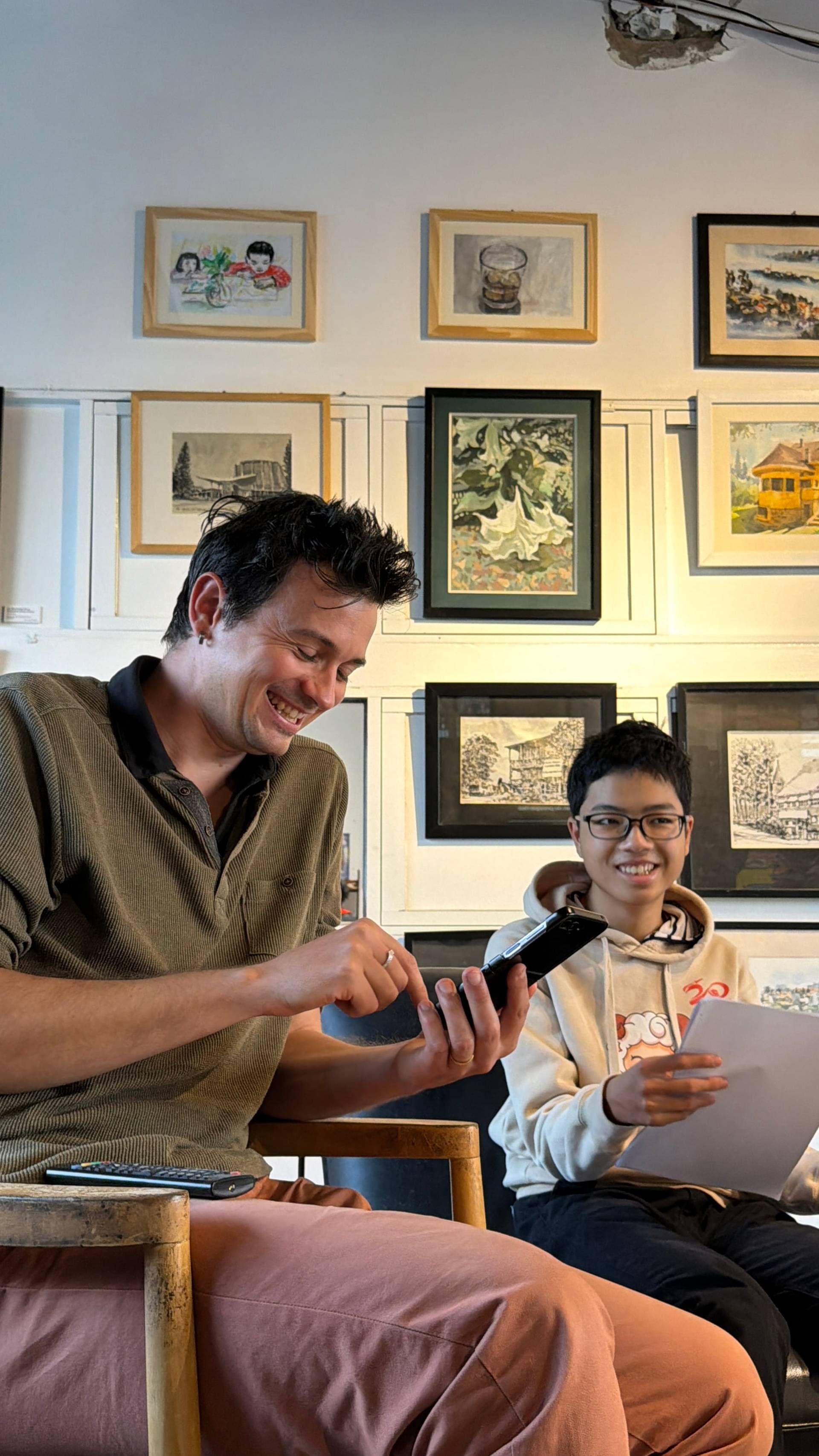 A joyful exchange in a Đà Lạt cultural venue, with two visitors engaging in conversation surrounded by Vietnamese artwork and gallery displays.