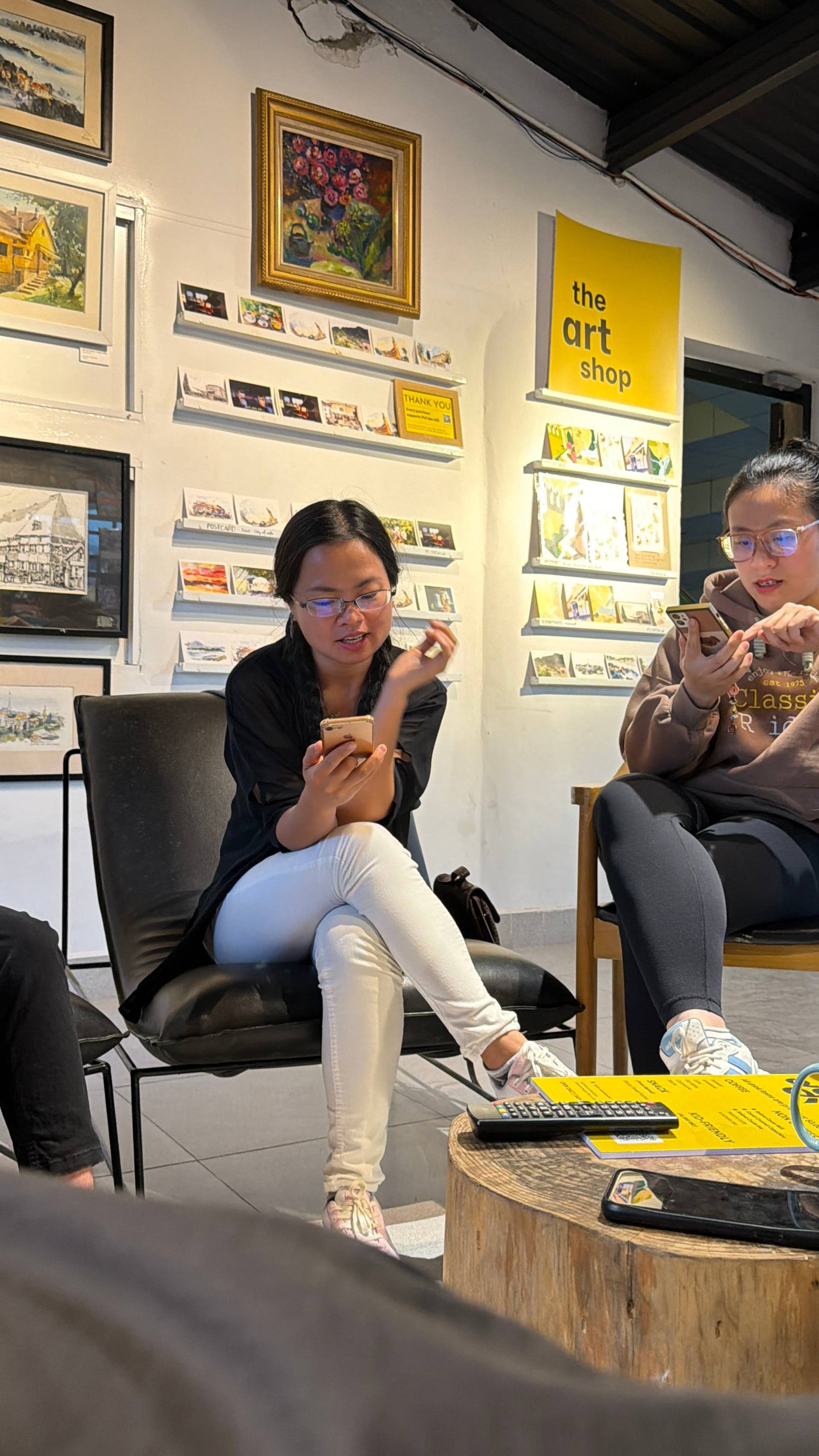 A social moment inside a Đà Lạt art gallery, where visitors enjoy the curated collection of Vietnamese artworks and prints displayed throughout the bright interior.
