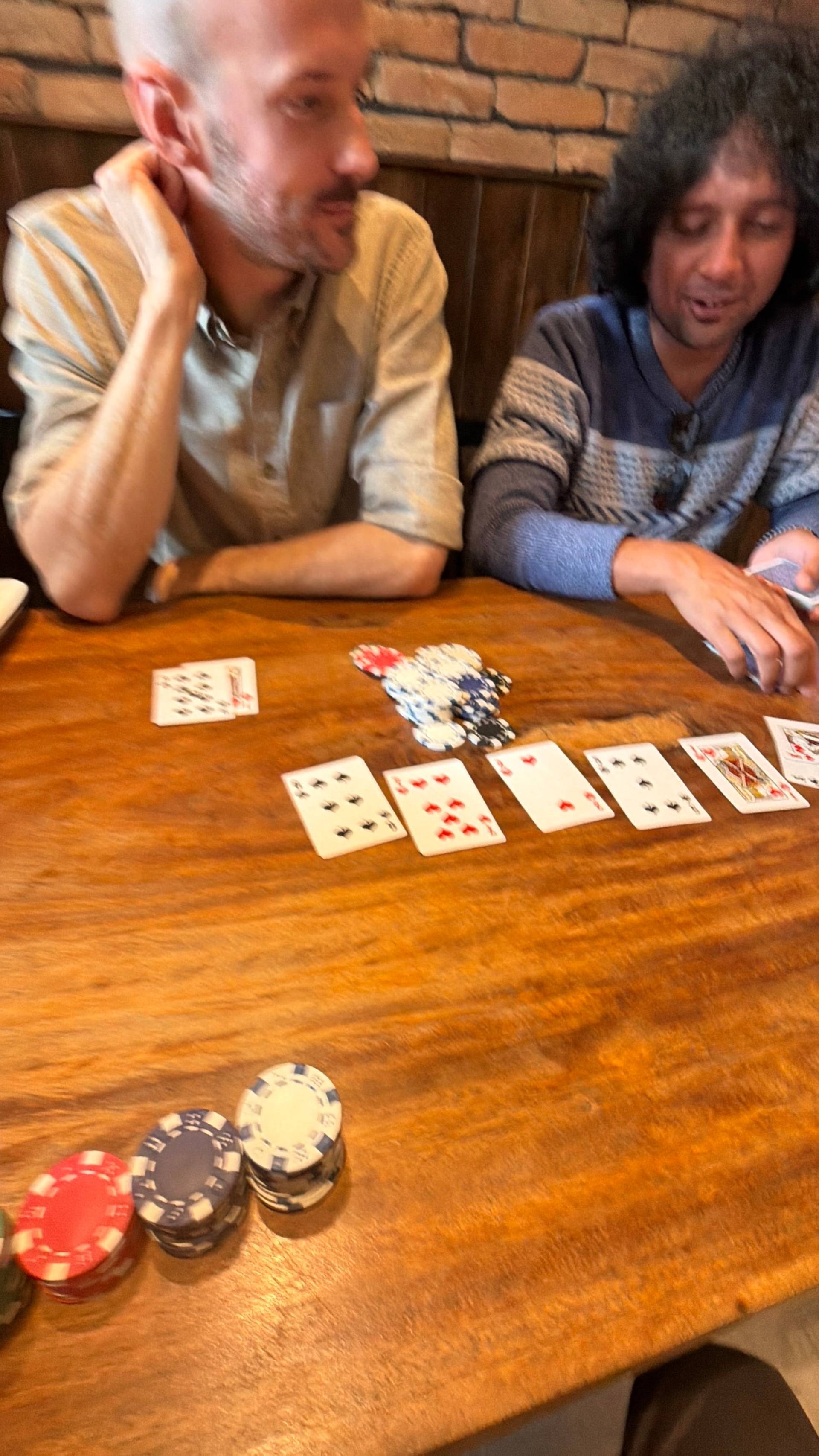 A close-up of a poker game in progress at a Đà Lạt cafe, showing cards and chips on a wooden table with players focused on gameplay.