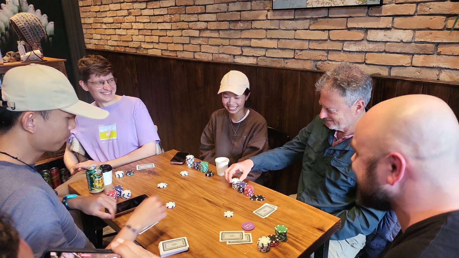 A multi-player poker game in progress at a rustic Đà Lạt establishment, with players gathered around a wooden table in a brick-walled interior.