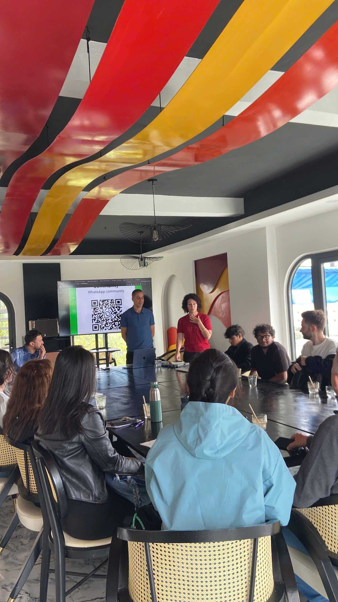 A vibrant meeting in Đà Lạt features a colorful ceiling design as attendees gather around a large table, engaging with presentations and discussions under natural light.