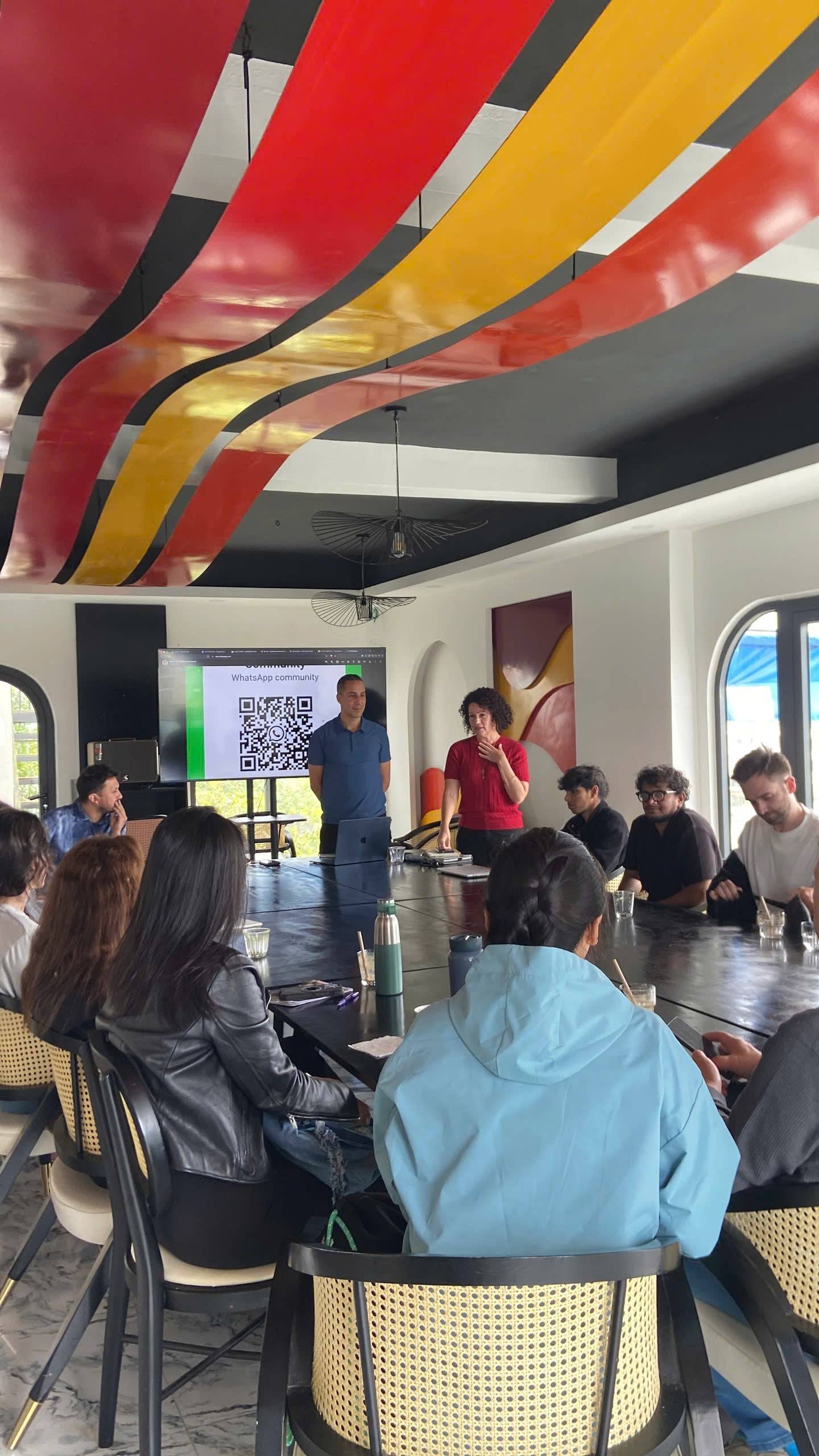 A vibrant meeting in Đà Lạt features a colorful ceiling design as participants gather around a large table, engaging with presentations and discussions.