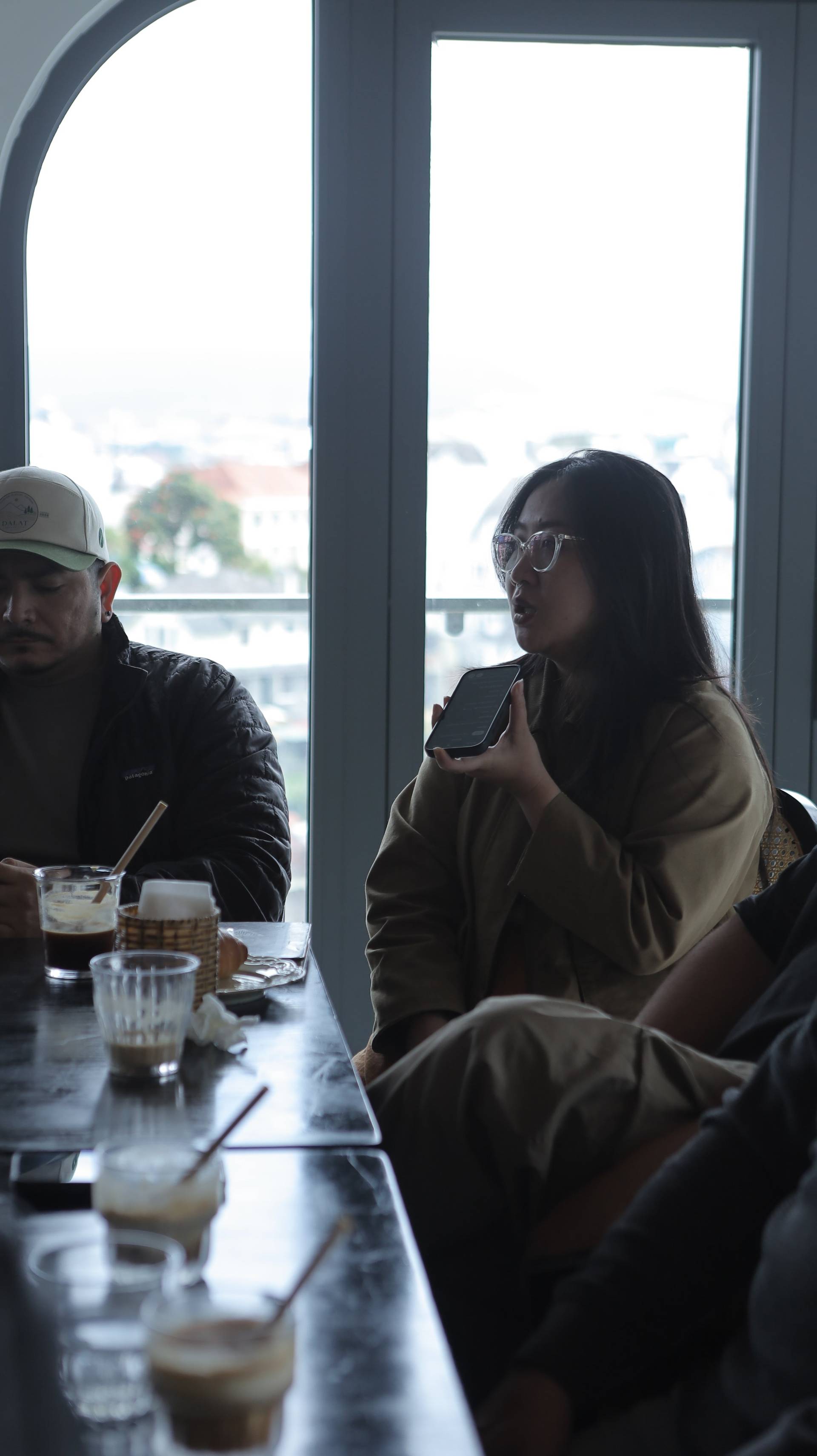 A group of friends enjoys a casual conversation over drinks in a cozy café with a scenic view of Đà Lạt's skyline.