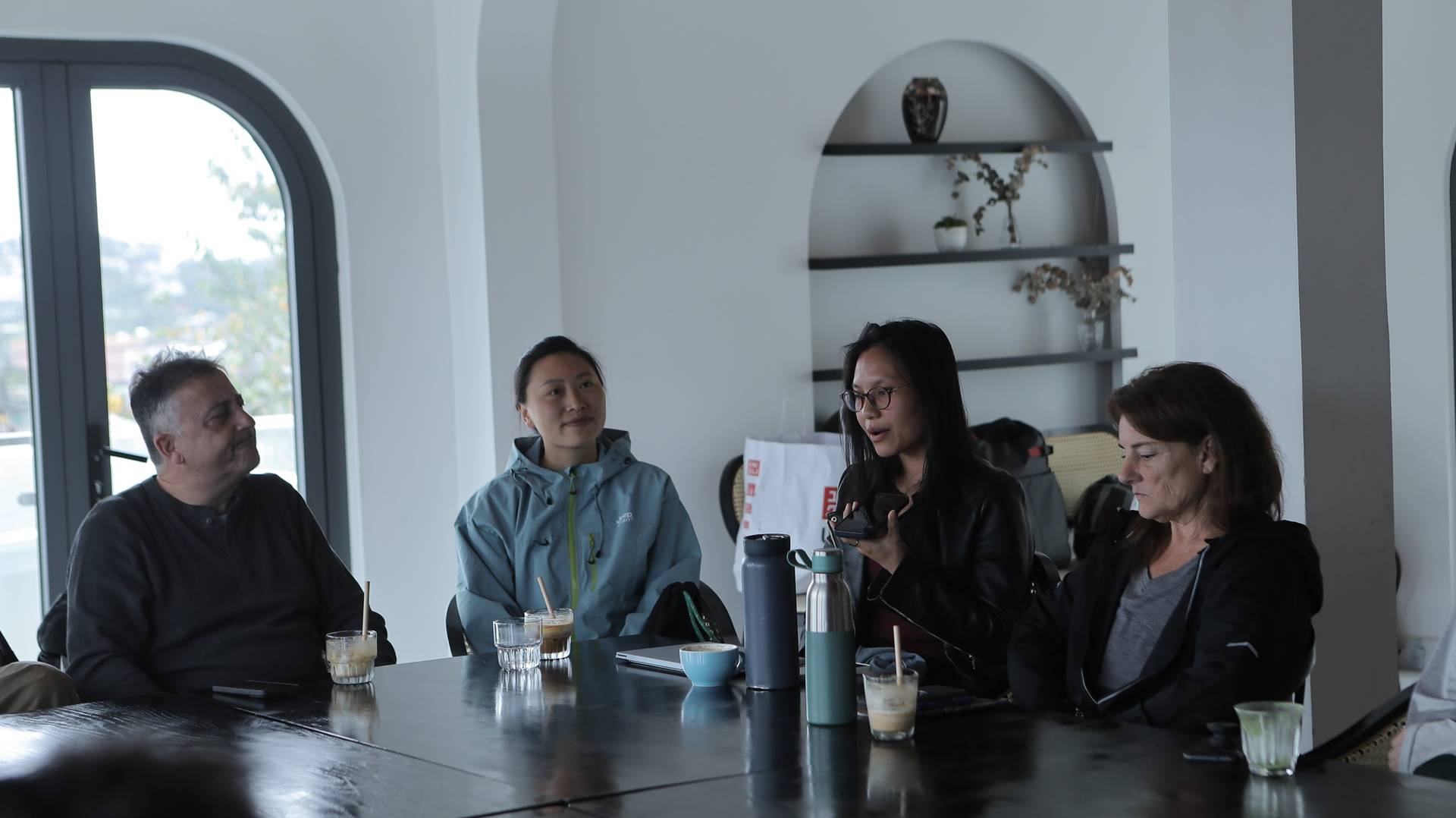 A group of people is gathered around a table in a cozy café setting in Đà Lạt, Vietnam, engaged in conversation and enjoying drinks.