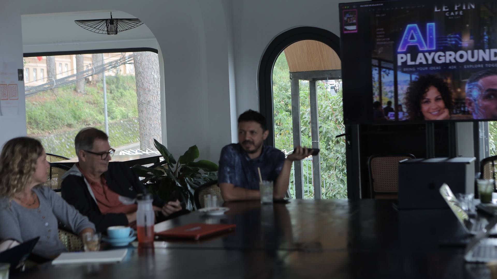 A group of people engaged in a discussion over drinks in a cozy café setting with scenic views and modern decor.