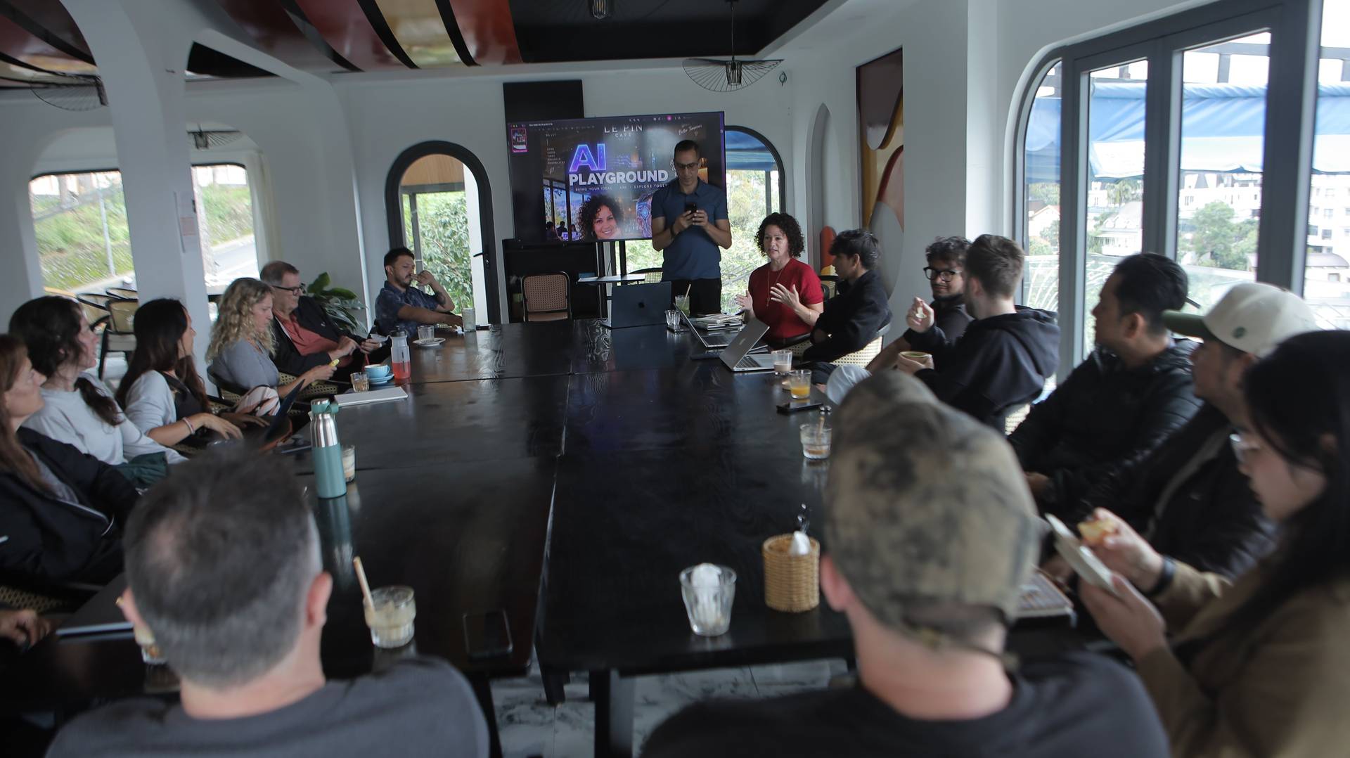 A group of professionals engaged in a collaborative discussion around a large table in a modern conference room with panoramic views of Đà Lạt's scenic landscape.