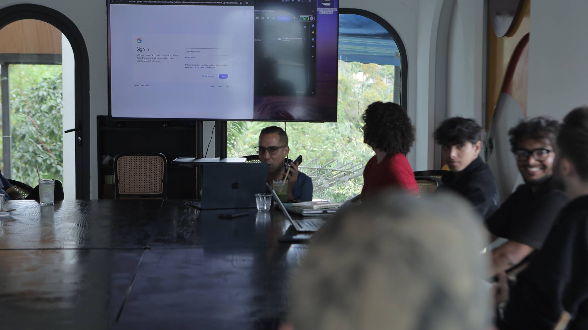 A group of individuals is gathered around a large table in Đà Lạt, Vietnam, engaged in what appears to be a collaborative meeting or presentation with a digital screen displaying a Google sign-in page.